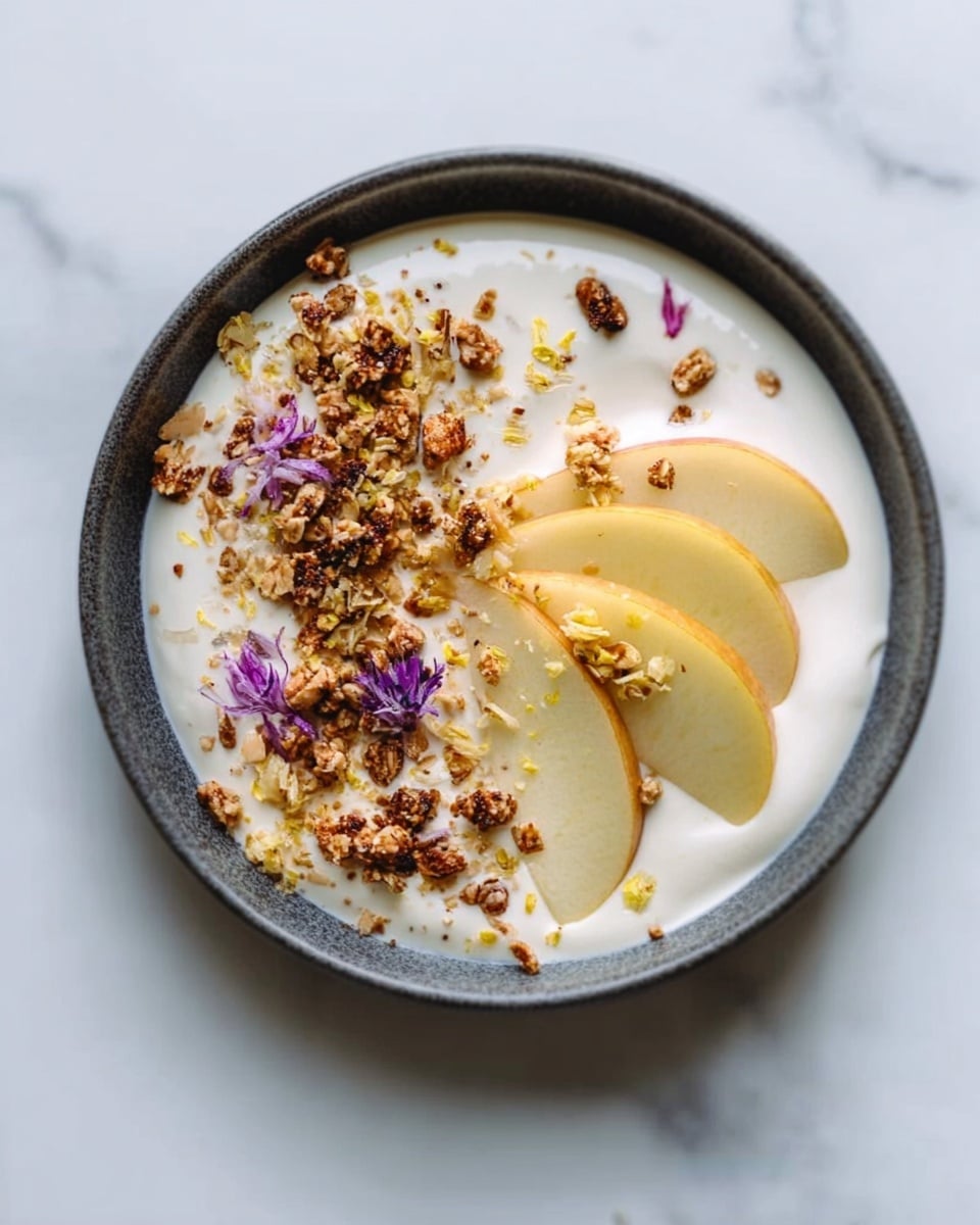 A white plate holds a creamy white base layer with a smooth texture spread evenly. On top, there are thin, curved slices of light yellow fruit arranged in a half-moon shape. Scattered over the fruit and cream are small clusters of brown crunchy bits, adding texture. Some tiny purple flower petals are sprinkled lightly on various parts of the dish. The surface below the plate is white marble. Photo taken with an iphone --ar 4:5 --v 7