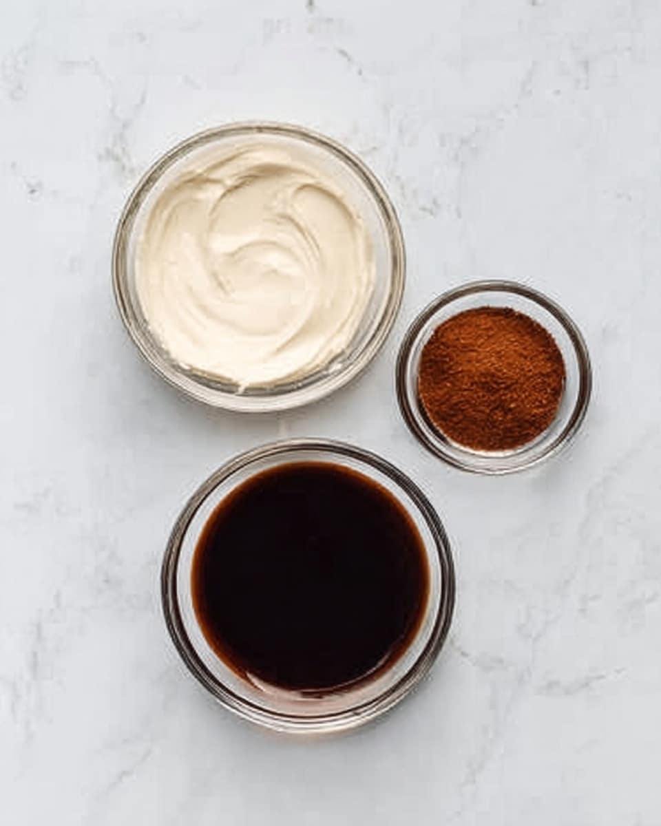 The image shows three glass bowls on a white marbled surface arranged in a triangle shape. The largest bowl at the bottom contains a dark brown liquid with a smooth texture. Above it, to the left, there is a medium-sized bowl filled with a thick, creamy white substance that is smooth on top. To the right of this, there is the smallest bowl holding a reddish-brown powder, looking fine and dry. The bowls are clear, round, and simple, showing the contents clearly. Photo taken with an iphone --ar 4:5 --v 7