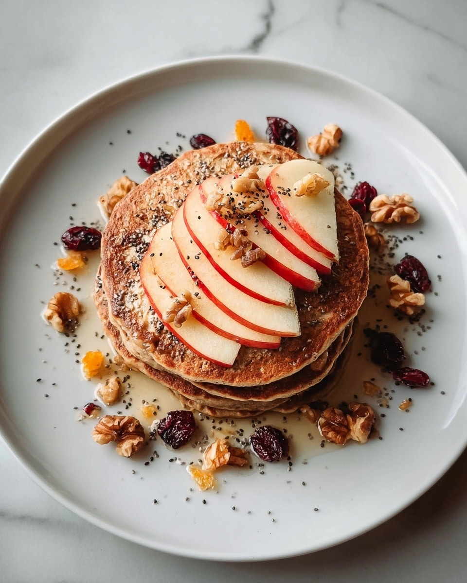 A stack of four light brown pancakes sits in the center of a white plate that is placed on a white marbled surface. On top of the pancakes, there is a neat fan of thin apple slices with red skin and white flesh. Around the apple slices, scattered walnut pieces, dried cranberries, and small orange dried fruit add texture and color contrast. Tiny black chia seeds are sprinkled over the stack and toppings, while a light drizzle of honey gives a slight shine to the whole dish. Photo taken with an iphone --ar 4:5 --v 7