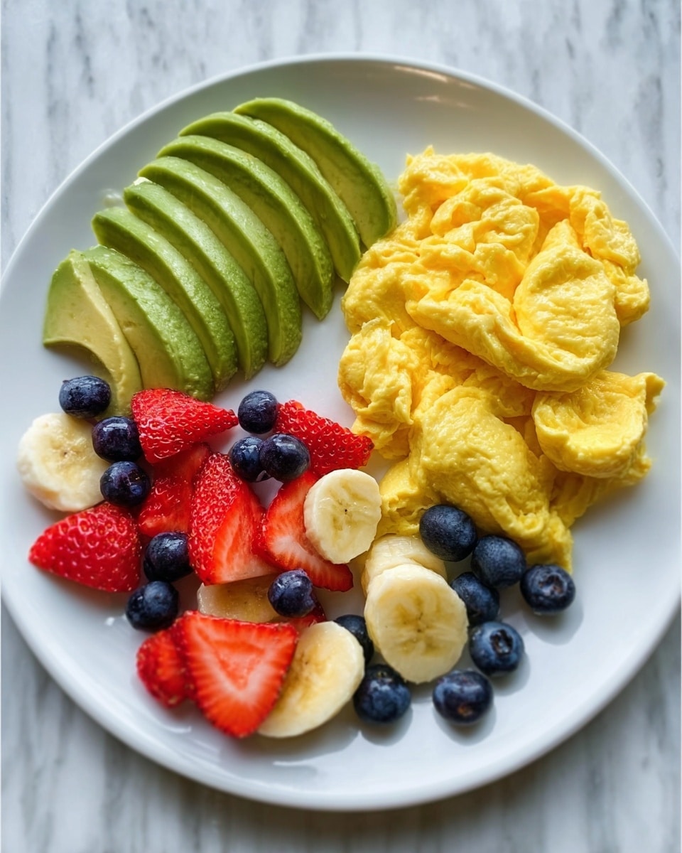 A white plate on a white marbled surface holds a colorful breakfast. On the left side, there is a fan of thinly sliced green avocado with smooth texture. Next to it on the right, there is a fluffy yellow scrambled egg stack with soft folds. In front of both, at the bottom of the plate, is a mix of fresh fruit chunks: round yellow banana slices, bright red strawberry pieces, and small blue blueberries scattered around. The colors contrast well with the white plate and marbled background. photo taken with an iphone --ar 4:5 --v 7