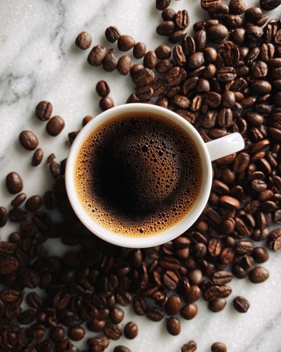A white cup filled with dark coffee that has a light foam on top, placed on a white marbled surface. Coffee beans are spread all around the cup, covering much of the surface. The scene shows a close-up view from above, highlighting the rich color of the coffee and the textured coffee beans. photo taken with an iphone --ar 4:5 --v 7