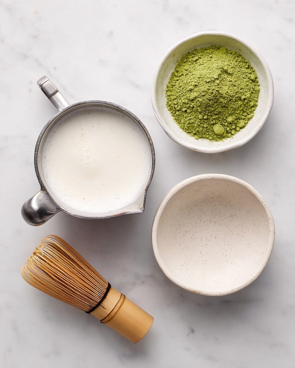 The image shows four items arranged on a white marbled surface: a metal measuring cup filled with frothy white liquid positioned on the left, a small white bowl containing bright green powder placed on the top right, an empty white speckled bowl located at the bottom right, and a bamboo whisk with thin bristles lying below the metal cup towards the lower left. The scene is clean and well-lit, focusing on the natural textures and colors of the items. photo taken with an iphone --ar 4:5 --v 7