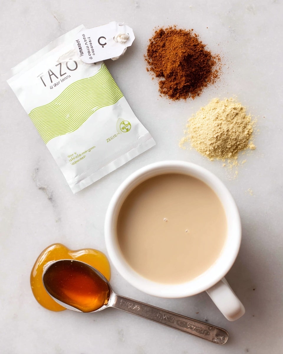 The image shows a white measuring cup filled with a smooth, light beige liquid positioned at the bottom right. Above it, there are two small piles of powdered spices; one is a dark brown color and the other is a pale yellow. Near the top left, there is a white tea bag with a tag labeled