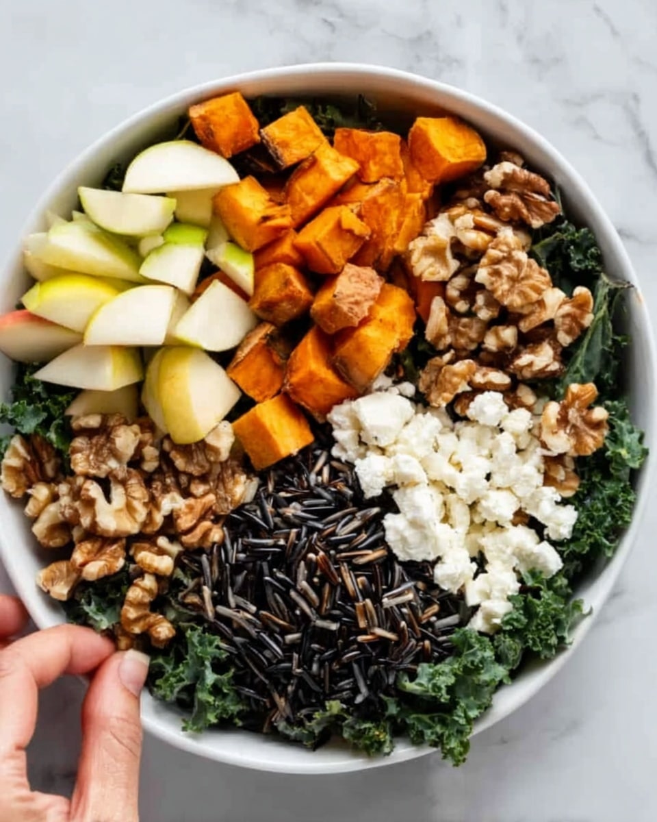 A white bowl filled with colorful layers of food sits on a white marbled surface. Starting from the left, there are small pale yellow and green apple pieces with smooth edges. Next to them, bright orange cubes of roasted sweet potato with a slightly rough texture fill a section. In the middle right part of the bowl, there is a dense pile of dark wild rice with a shiny surface. Above the rice, from left to right, there is a mix of white cottage cheese with a soft, lumpy texture, and light brown chopped walnuts that appear crunchy. The base of the bowl is lined with fresh dark green leafy kale providing a rich background. A woman's hand is seen reaching toward the bowl. photo taken with an iphone --ar 4:5 --v 7