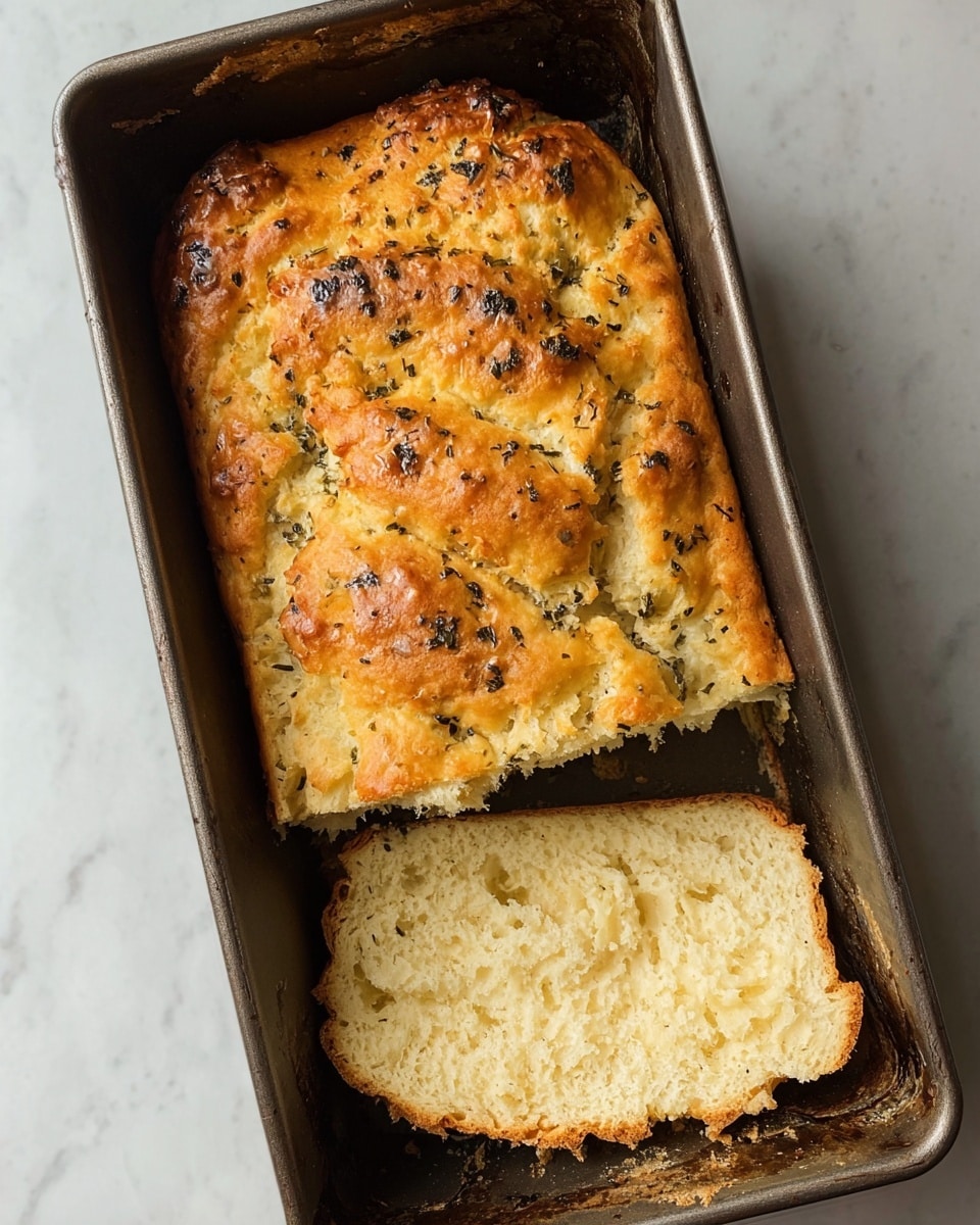 A rectangular bread loaf in a metal baking pan is shown with a slice cut and set slightly out of the pan, revealing a soft and fluffy inside with an open crumb texture. The top crust is golden brown with some darker spots and is sprinkled with small bits of herbs, giving a rough surface look. The bread’s color ranges from light beige inside to a rich golden-brown crust on top, with the herbs adding dark green dotting across the loaf. The baking pan appears slightly worn with baked-on residue along the edges, and the image is set on a white marbled surface. photo taken with an iphone --ar 4:5 --v 7