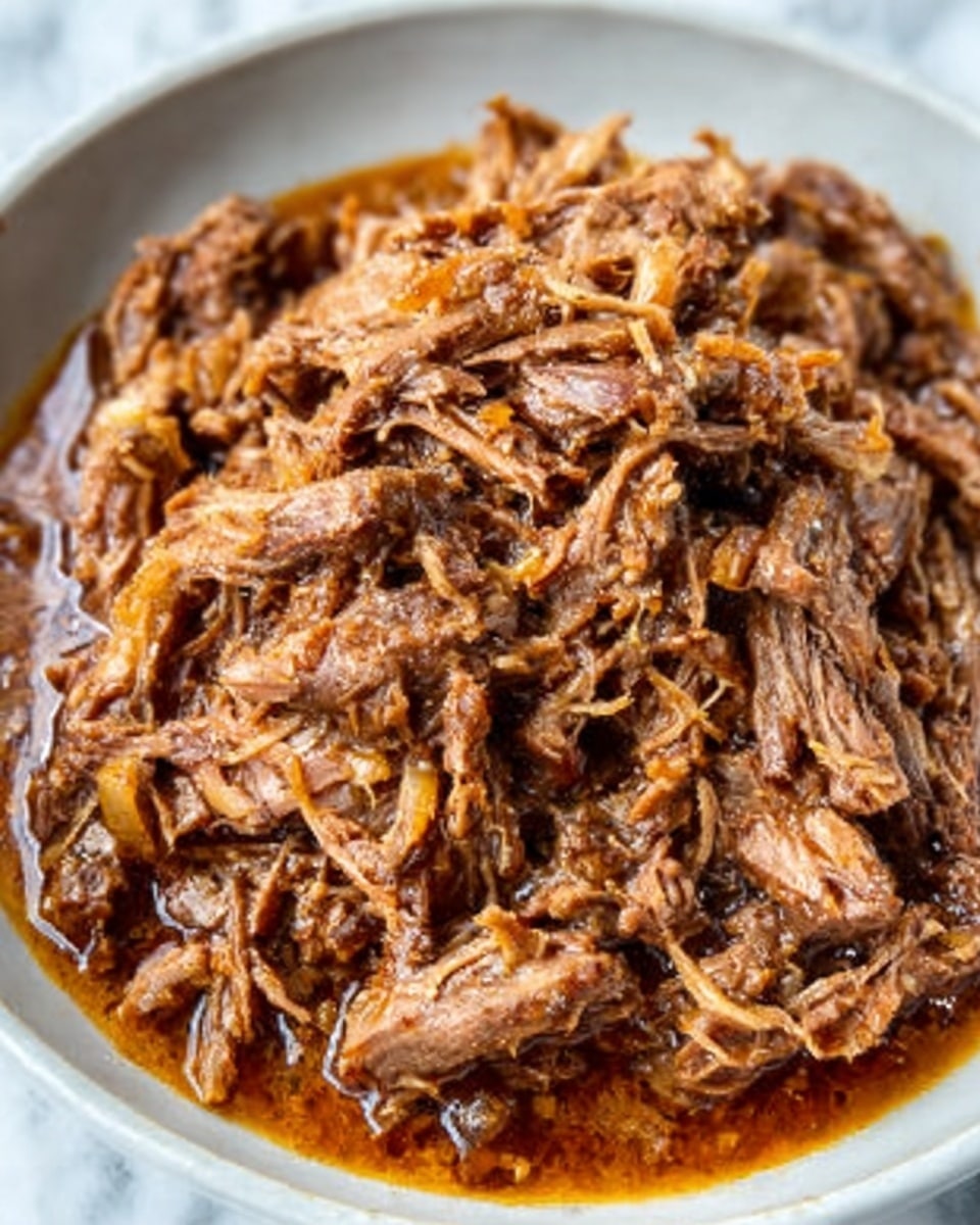 The image shows a close-up view of a dish filled with shredded meat soaked in a rich, brown sauce that looks juicy and tender. The meat pieces are small and stringy, mixed with bits of soft onions and spices, sitting in a white bowl. The dish has a rustic texture with visible layers of meat fibers and a slight shine from the sauce. The background is a white marbled surface, giving the image a fresh and clean look. Photo taken with an iphone --ar 4:5 --v 7