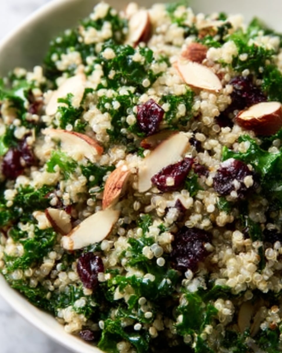 A close-up view of a quinoa salad in a white bowl showing three main layers: a fluffy base of small, round white quinoa grains with some translucency, mixed throughout with small dark specks; the middle layer contains bright green kale leaves with a slightly crinkled texture spread evenly, mixed with thin pale beige almond slices scattered on top; the top layer has dark red dried cranberries spread throughout, adding pops of deep color. The salad has a fresh and textured look with a variety of sizes and shapes from the quinoa, kale, almonds, and cranberries, sitting on a white marbled surface. photo taken with an iphone --ar 4:5 --v 7