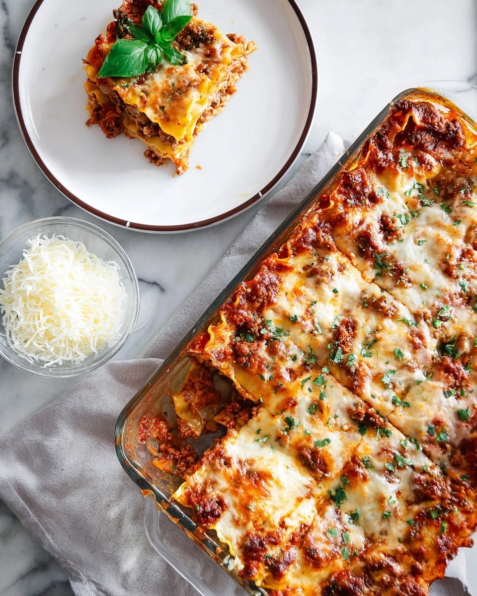 This image shows a glass baking dish filled with a layered lasagna that has a golden brown melted cheese top sprinkled with small green herb pieces. The lasagna has visible layers of flat yellow pasta sheets, reddish meat sauce, and melted creamy cheese underneath. To the top left on a white plate with a thin dark rim sits a square slice of the lasagna garnished with fresh green basil leaves. Near the plate, there is a small clear bowl of white shredded cheese. The whole setup is on a white marbled surface with a light gray cloth underneath the plate. Photo taken with an iphone --ar 4:5 --v 7
