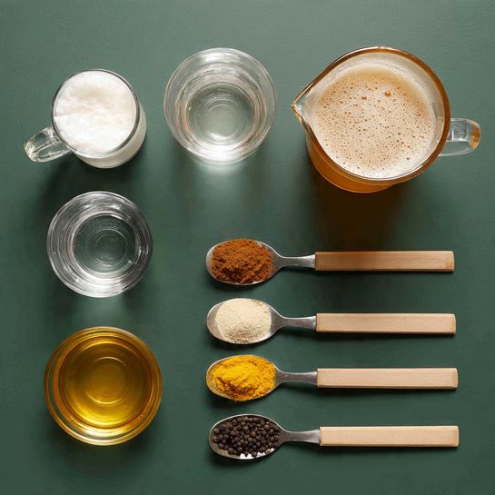 The image shows six ingredients arranged neatly on a dark green surface. On the top right, there is a clear glass pitcher filled with a light brown frothy liquid. To its left, a smaller glass pitcher holds a white foamy liquid. Below them, a tiny clear glass contains a transparent liquid. Beneath that is a small round clear bowl filled with golden honey. On the right side of the image, four spoons are stacked horizontally, one below the other, each with a light wooden handle and silver scoop. From top to bottom, they carry dark brown powder, light beige powder, black pepper, and bright yellow turmeric powder. The entire setup is neat and evenly spaced. photo taken with an iphone --ar 4:5 --v 7