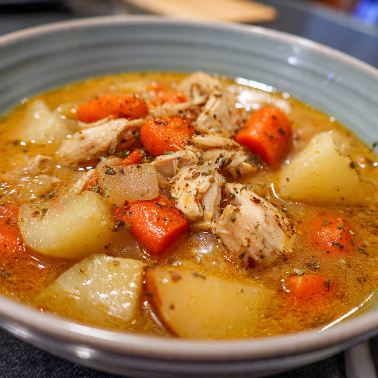 A close-up view of a white bowl filled with creamy chicken soup, showing chunks of white chicken pieces, bright orange carrot slices, and small green peas all mixed in a light creamy broth. A yellow-handled spoon is scooping the soup, held by a woman's hand, and the bowl sits on a white marbled surface with a yellow cloth with white dots beside it. Photo taken with an iphone --ar 4:5 --v 7