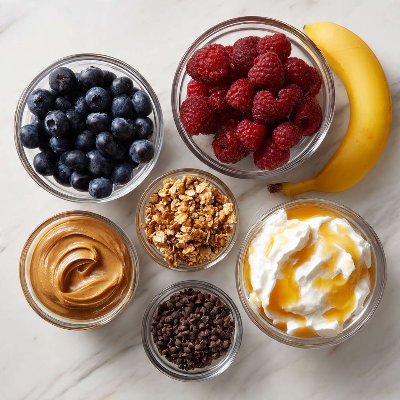 There are six clear glass bowls with different items arranged on a white marbled surface. Starting from the top left, one bowl holds fresh blueberries that are dark blue with a smooth texture. Next to it on the right is a bowl filled with red raspberries that have a soft and bumpy texture. To the far right is a bowl containing white cottage cheese mixed with golden honey, showing a creamy white and shiny yellow layered texture. Below these, on the left, there is a small bowl with smooth peanut butter in a light brown color. Next to it in the middle is a bowl of granola made of small crunchy clusters in light brown shades. Below and to the left is a very small bowl holding dark brown cacao nibs with a rough and bumpy texture. To the right of all bowls is a single, whole banana with a bright yellow peel. photo taken with an iphone --ar 4:5 --v 7