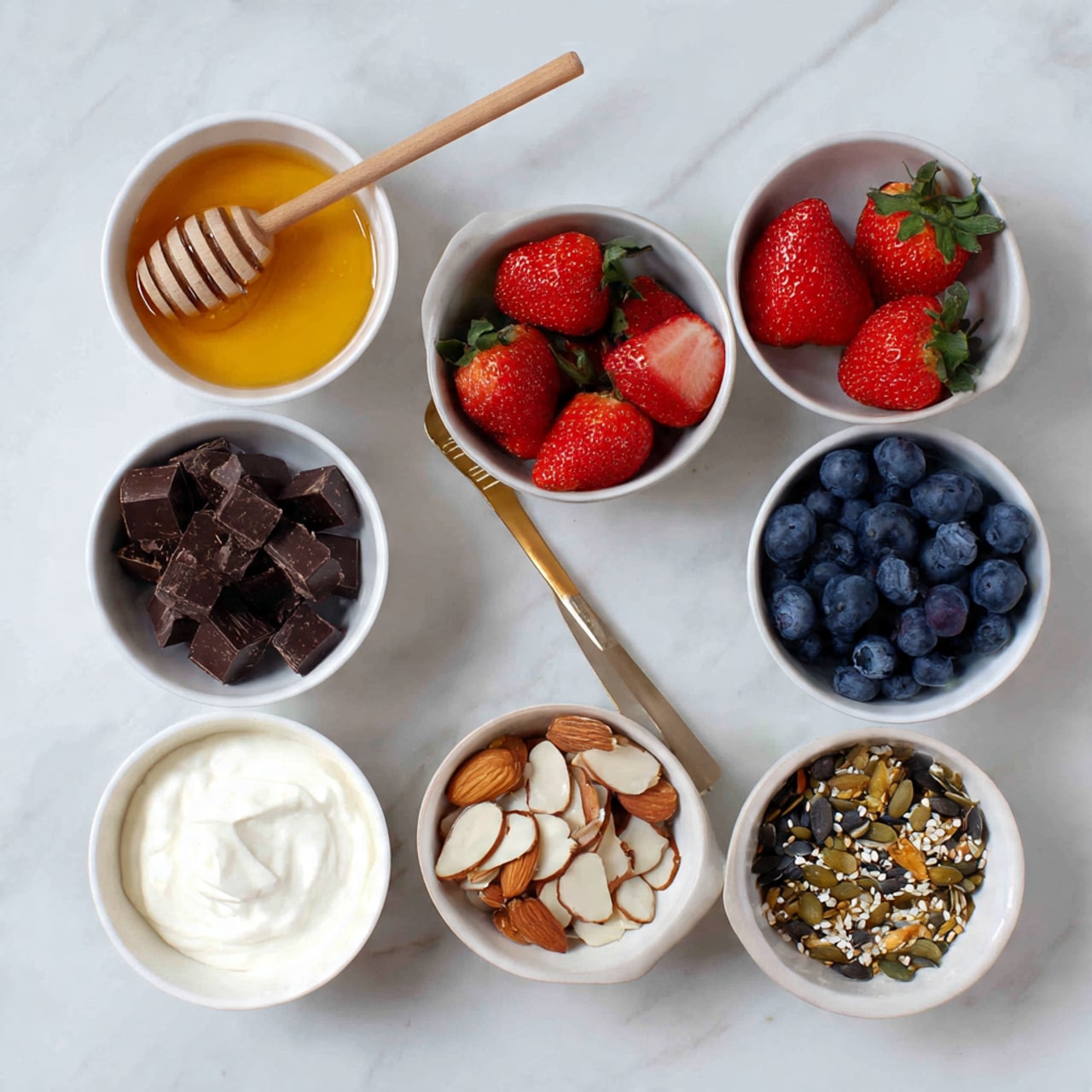 The image shows seven white bowls arranged on a white marbled surface. Starting from the top left, the first bowl holds golden honey with a wooden honey dipper resting inside it. To the right, a bowl is full of fresh whole strawberries with one sliced in half. Below that, there is a bowl with dark chocolate pieces in small chunks. To the right of the chocolate, a bowl contains plump blueberries. On the bottom left, a bowl is filled with white creamy yogurt with a smooth texture. Next to the yogurt, a bowl contains almond slices mixed with seeds. The colors are bright and natural, with a clear white and marbled background. photo taken with an iphone --ar 4:5 --v 7
