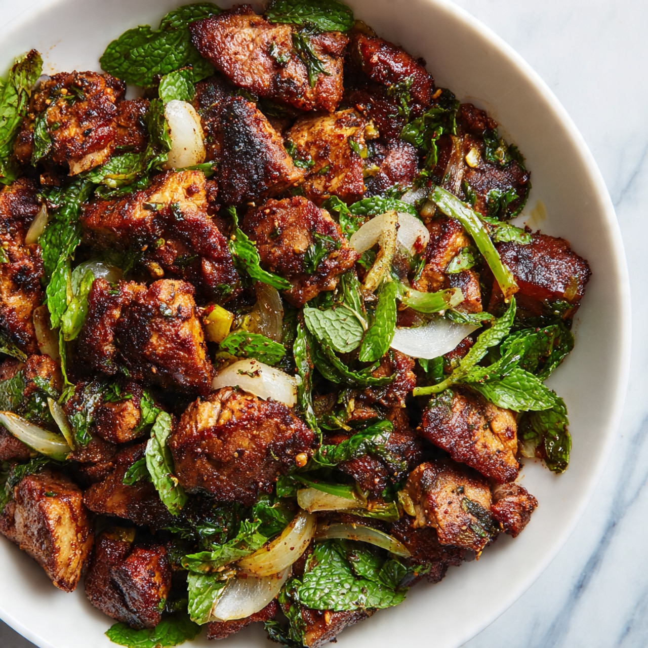 The image shows a close-up of a pile of spiced grilled meat pieces in a white bowl, mixed with fresh green mint leaves, chopped green onions, and small onion slices. The meat pieces are brown with a slightly charred texture and are sprinkled with visible spices, giving them a rough appearance. The fresh herbs add bright green colors and contrast with the meat, while the onion slices add a pale pink and white touch throughout the dish. The bowl sits on a white marbled surface with a blurred blue background. photo taken with an iphone --ar 4:5 --v 7