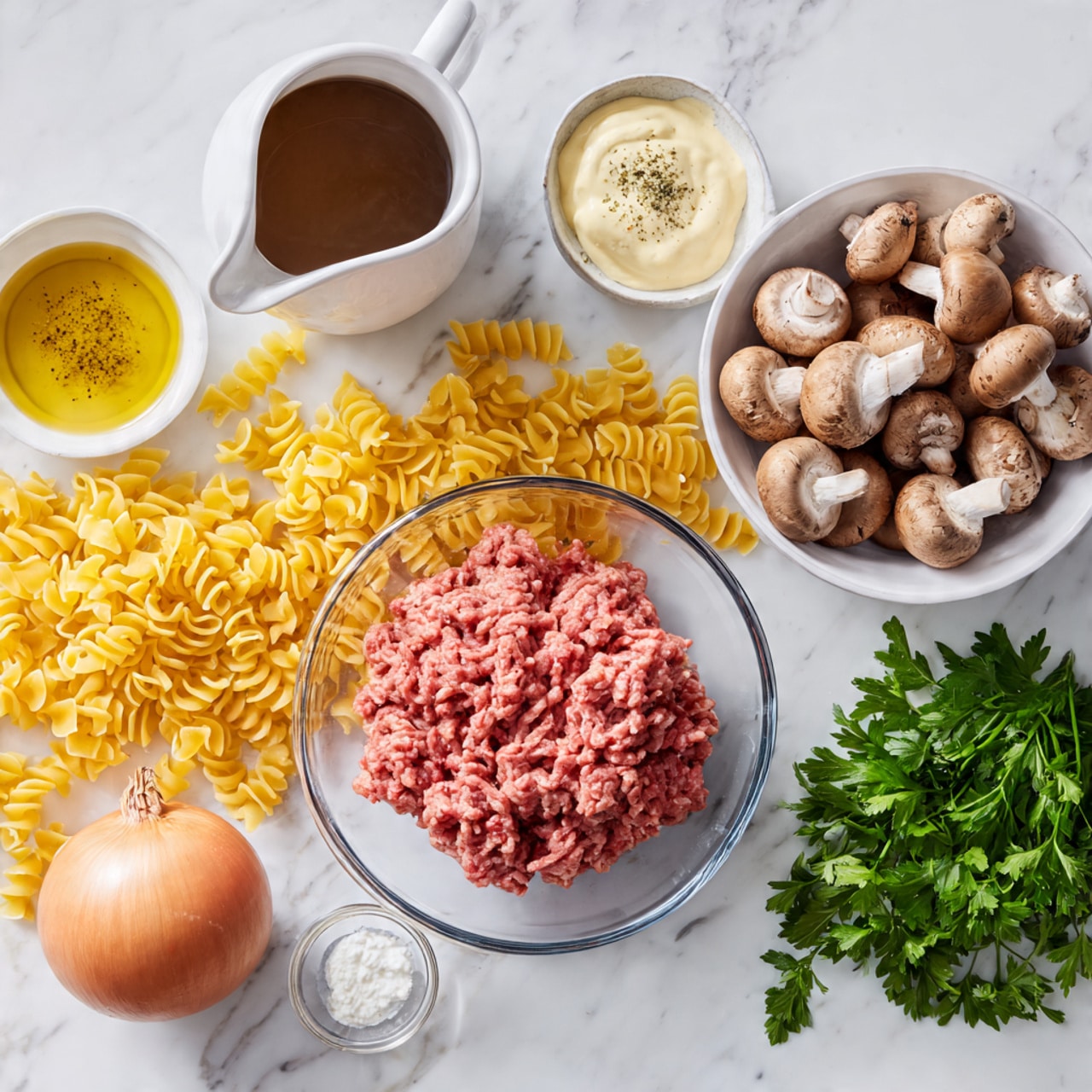 The image shows raw ground meat in a clear glass bowl placed on a white marbled surface scattered with uncooked yellow pasta. Nearby, there is a white jug with a creamy white liquid, a clear glass measuring cup filled with dark brown broth, and three small white bowls containing light brown mustard, olive oil, and white sour cream. To the right, an orange onion and fresh green parsley sit next to a white bowl filled with whole and sliced brown mushrooms. Photo taken with an iphone --ar 4:5 --v 7