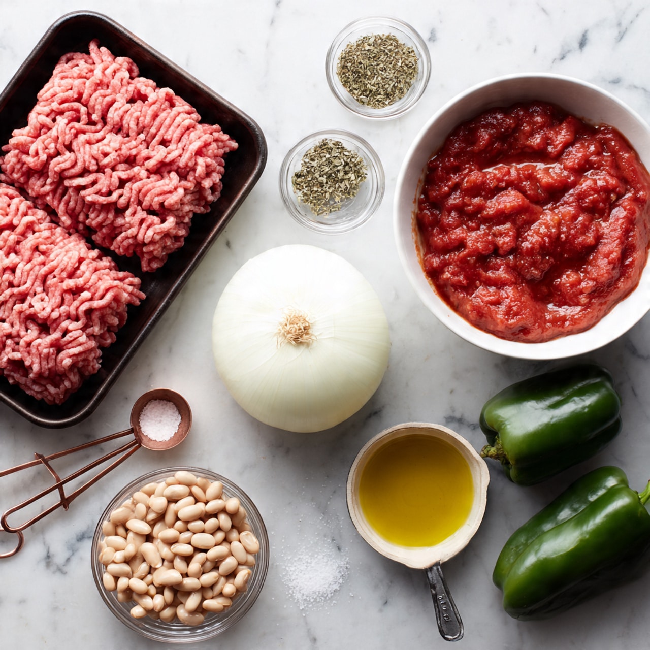 A top view image showing raw pink ground meat with white fat specks in a black tray at the top left, a white half onion with smooth layers at the center, a white bowl with chunky red tomatoes in sauce on the right, and a red colander with light beige beans at the bottom left. Two green bell peppers and a white garlic bulb lie on the white marbled surface. Nearby, there are two small glass bowls with green dried herbs, one small glass bowl of yellow olive oil, and a set of copper measuring spoons holding salt on the white marbled surface. Photo taken with an iphone --ar 4:5 --v 7