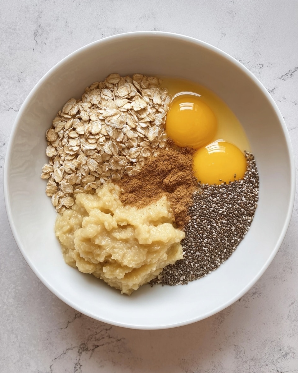 A white bowl on a white marbled surface holds four separate layers of ingredients. On the top left is a light beige pile of dry oats with a rough texture. To the right of the oats are two bright yellow raw egg yolks with clear egg whites surrounding them. Below the yolks is a small pile of ground brown cinnamon powder. On the bottom left, there is a mound of mashed banana with a soft, mushy texture in a pale yellow shade. In the center, resting between the oats, eggs, and banana, is a small pile of dark gray chia seeds with a shiny surface. Photo taken with an iphone --ar 4:5 --v 7