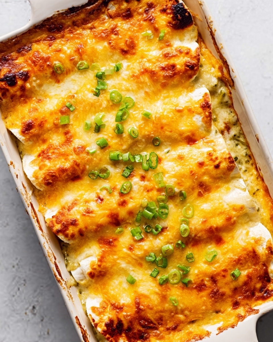 The image shows a white rectangular dish filled with baked enchiladas covered in melted golden-brown cheese. There are five rolled enchiladas arranged side by side, with the cheese bubbling on top. The enchiladas have a light creamy sauce under the cheese, visible where the cheese has melted unevenly. Small green onion slices are sprinkled evenly over the top, adding a fresh pop of color against the warm cheese. The edges of the dish are clean, and the background is a white marbled surface. photo taken with an iphone --ar 4:5 --v 7