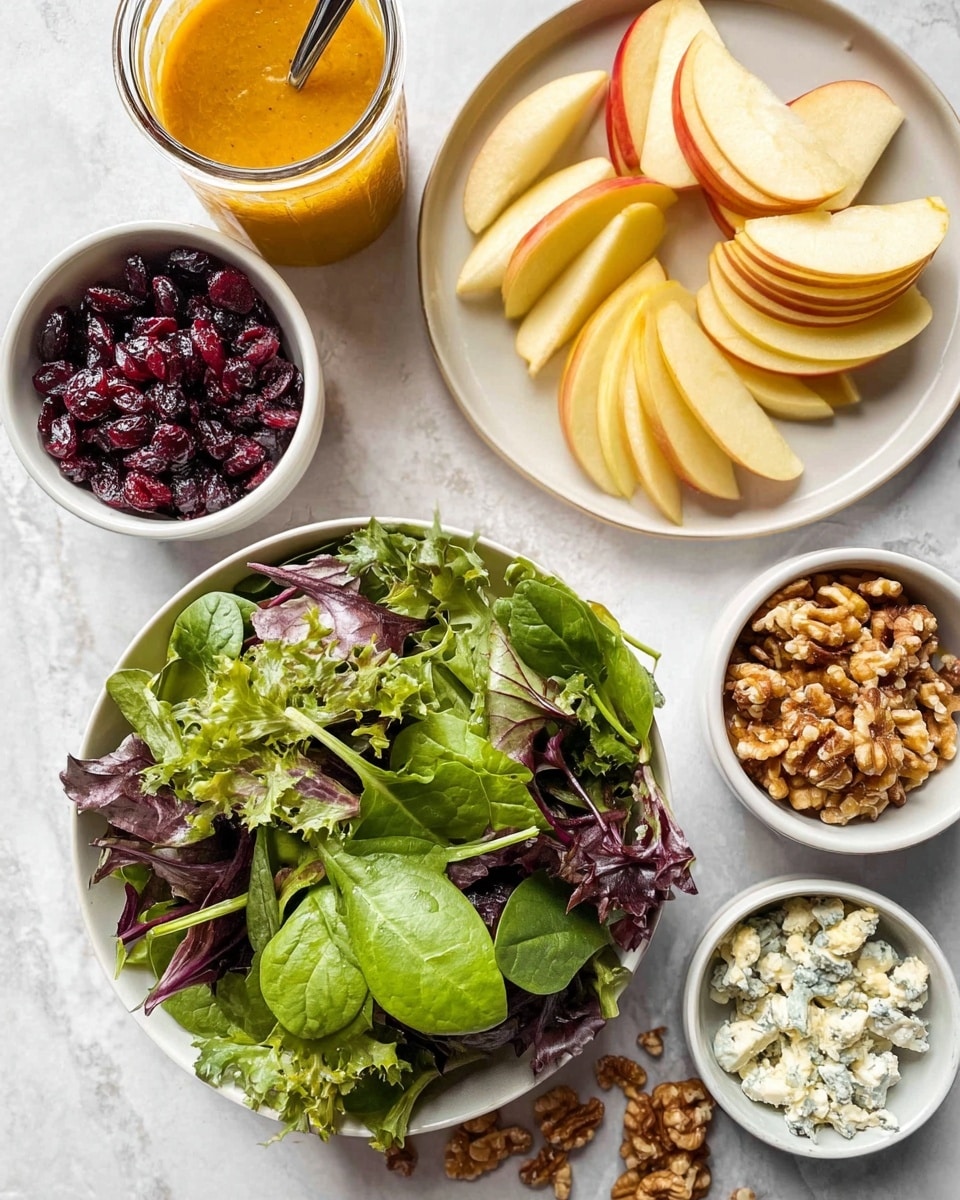 A white bowl holds mixed green leafy salad that has dark purple and bright green leaves with different shapes and textures, mostly smooth spinach-like and some frilly edges; above it to the right, a white plate contains thinly sliced apple pieces arranged fanned out, showing yellow and red skin and pale flesh; at the top left, a small white bowl is filled with dark red dried cranberries, and next to it is a glass jar with orange-colored dressing and a spoon sticking out; on the right side, two small white bowls sit near each other, one with chopped walnut pieces and a few scattered outside, the other with light blue crumbly cheese; all items are placed on a white marbled textured surface photo taken with an iphone --ar 4:5 --v 7