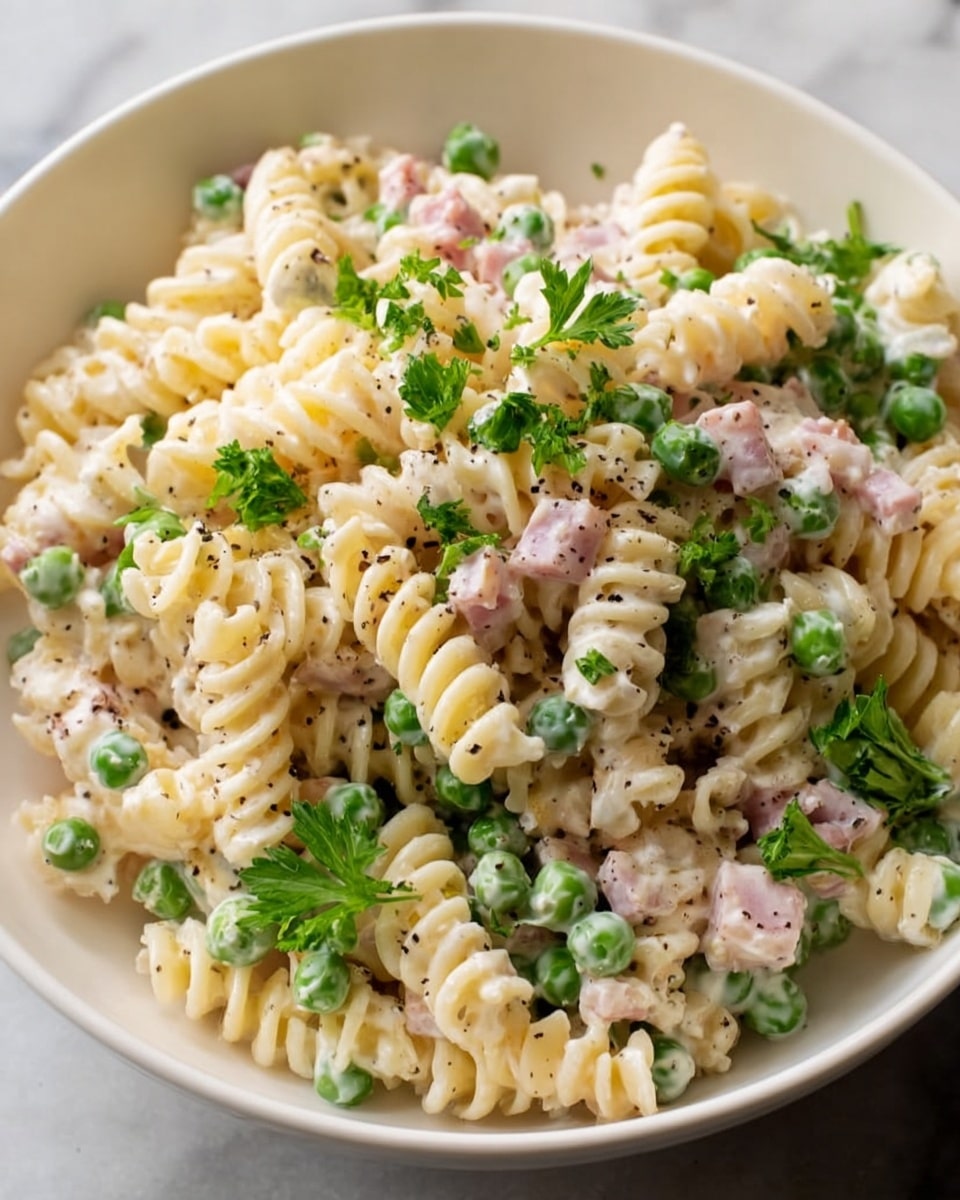 A close-up view of a white bowl filled with creamy rotini pasta, mixed with small green peas and small pieces of pink ham. The pasta is coated in a white creamy sauce, with visible black pepper sprinkled on top. Bright green fresh parsley leaves are scattered over the dish, adding a fresh touch. The bowl sits on a white marbled surface. Photo taken with an iphone --ar 4:5 --v 7