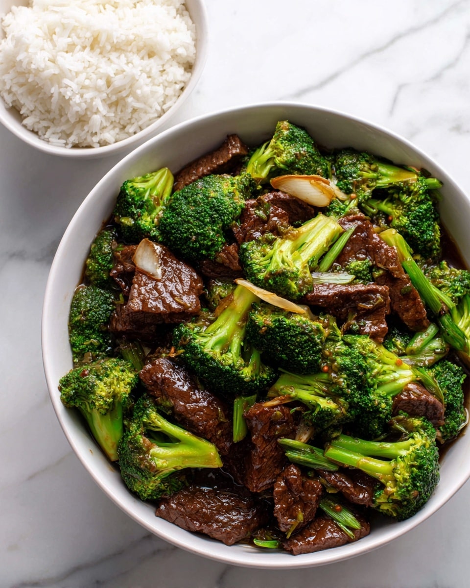The image shows a bowl filled with stir-fried beef and broccoli. The bowl is white and contains chopped pieces of beef with a dark brown sauce, bright green broccoli florets, and light brown slices of garlic or onion mixed in. The beef looks tender and shiny from the sauce, while the broccoli appears fresh and slightly crisp. Next to the bowl is a smaller white bowl with plain white rice. The surface underneath everything is a white marble texture. Photo taken with an iphone --ar 4:5 --v 7