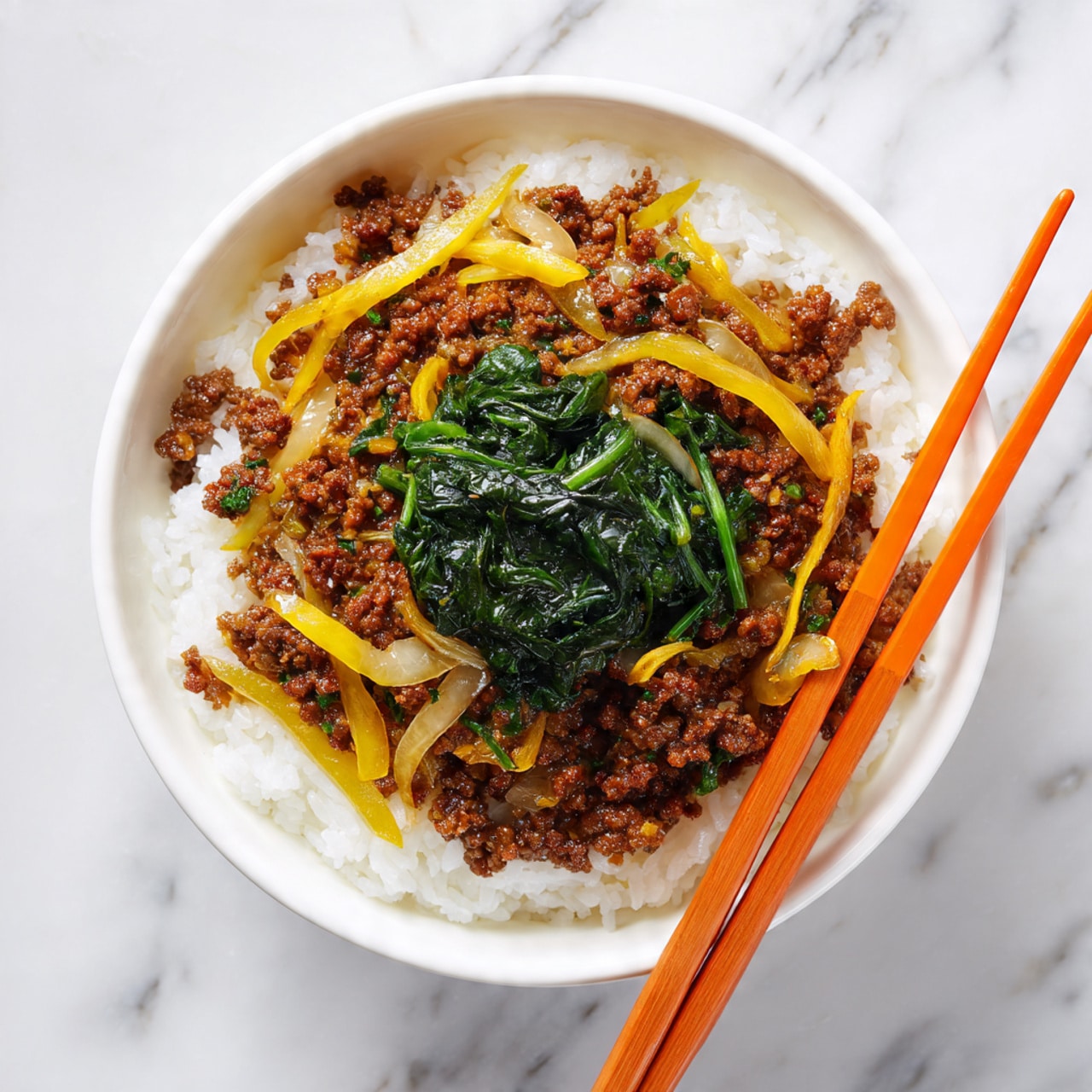 A white bowl contains a base layer of soft white rice, topped with a savory mixture of cooked minced meat and thin slices of cooked onions and yellow vegetables. In the center, a small pile of dark green leafy vegetable adds color contrast. Bright red chopsticks rest on the rim of the bowl, placed diagonally. The bowl is set on a white marbled surface. photo taken with an iphone --ar 4:5 --v 7