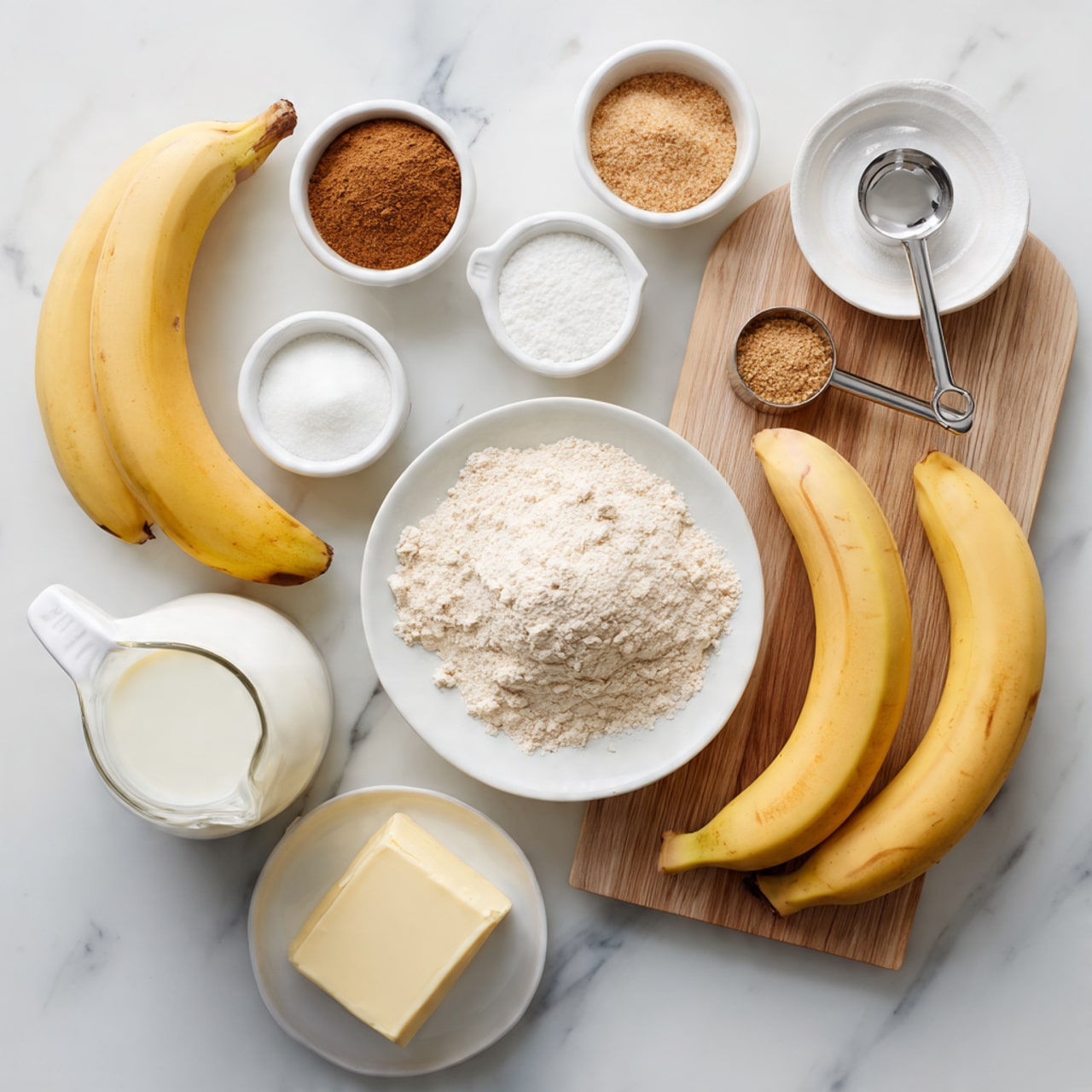 The image shows an overhead view of baking ingredients neatly arranged on a white marbled surface. There are two ripe bananas, one peeled and one unpeeled, placed on a light wooden board to the right. Surrounding them are various small white dishes and measuring cups filled with different ingredients: a small white plate with white powder and brown cinnamon, a small white bowl and a white measuring cup with brown sugar, a white measuring cup with white flour, and a silver measuring cup with a light brown powder. A glass jug of white milk sits next to the bananas, and a white butter dish holds a rectangular stick of butter near the bottom left. Photo taken with an iphone --ar 4:5 --v 7