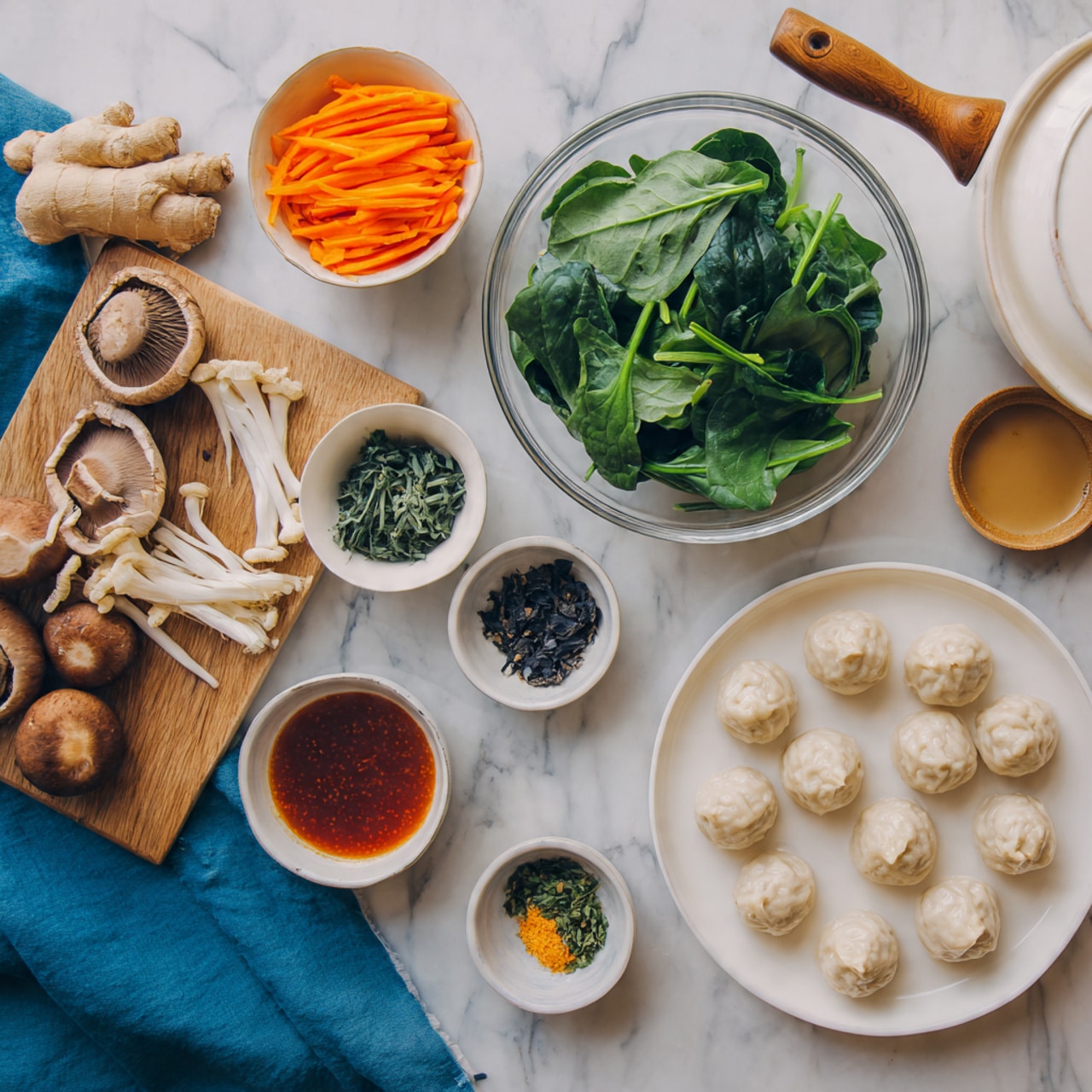 The image shows a white marble surface with ingredients arranged neatly: a white plate with light beige dumplings on the right, a clear bowl filled with green spinach leaves above it, and a smaller white bowl holding thin orange carrot strips on the top left. Scattered around are light brown mushrooms, a piece of fresh ginger, a blue cloth, and small white bowls containing dark leafy herbs, a dark red sauce, and a light brown liquid. There is also a white pot with a wooden handle visible at the top right. Photo taken with an iphone --ar 4:5 --v 7