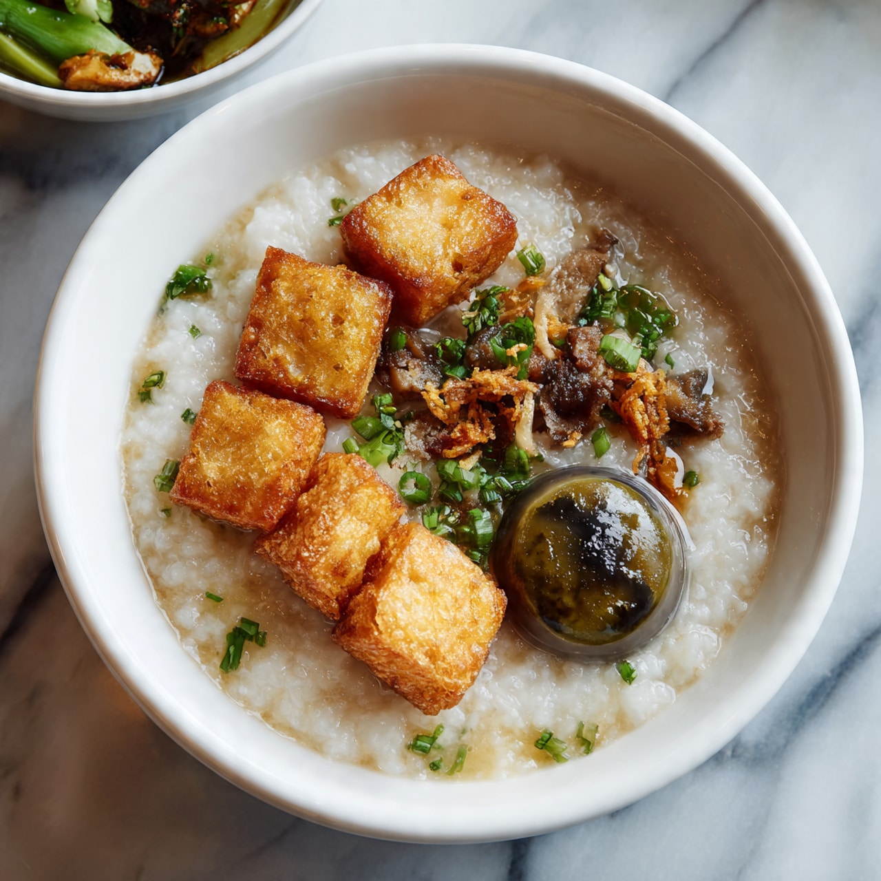 A white bowl filled with smooth white rice at the bottom, topped with four halves of soft-boiled eggs with bright orange yolks arranged on one side. On the opposite side, there is a small amount of green sauce or paste with a few black sesame seeds scattered around it and on the rice. The bowl sits on a white marbled surface next to a pink ridged item partially visible. The photo taken with an iphone --ar 4:5 --v 7