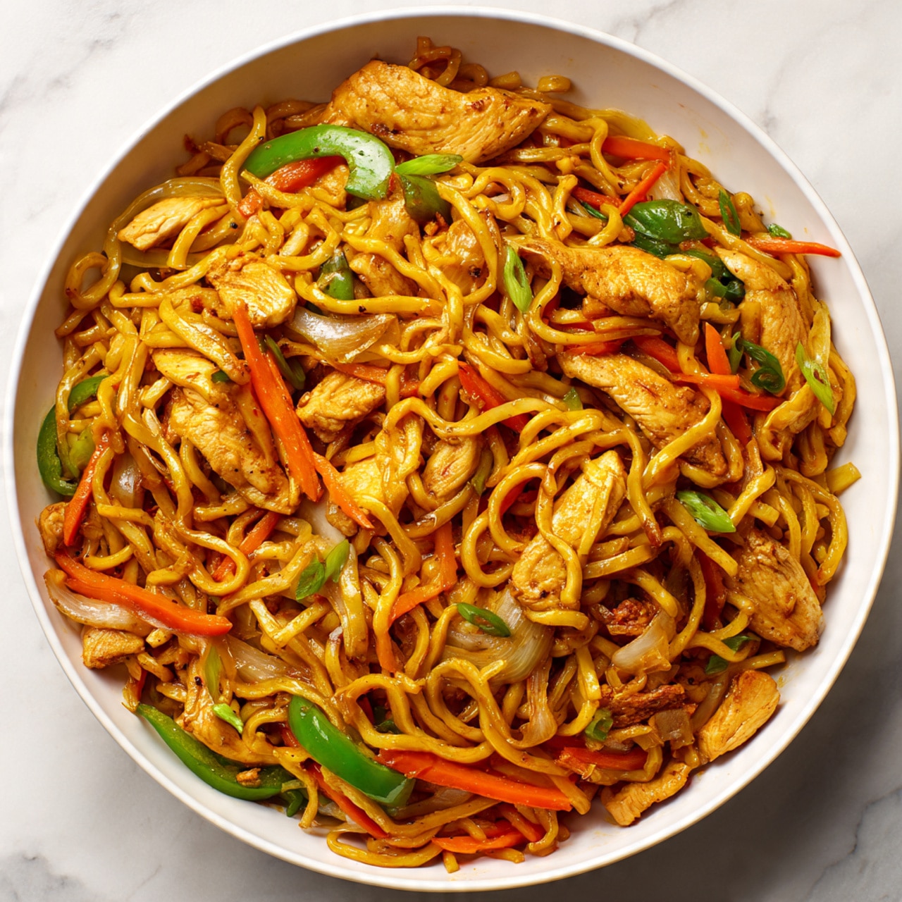 A large white bowl filled with stir-fried noodles that are golden-brown and shiny, mixed with thin orange carrot strips and green bell pepper slices. There are several light brown, cooked pieces of chicken scattered on top and mixed throughout. The sauce gives the noodles a glistening look, and the dish is placed on a white marbled surface. The image is close-up, showing the texture of the noodles and vegetables clearly. Photo taken with an iphone --ar 4:5 --v 7