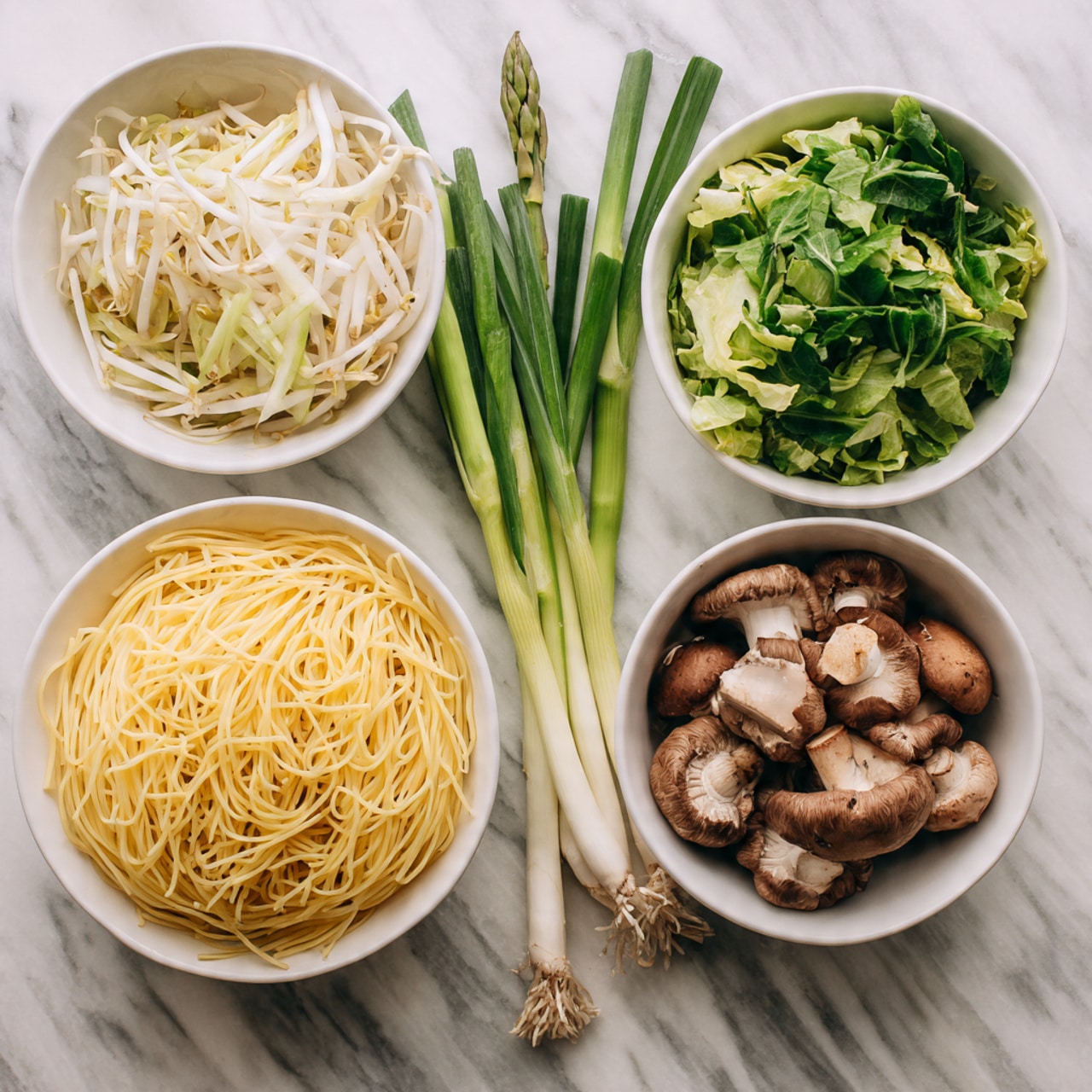 The image shows four white bowls on a white marbled surface filled with different ingredients arranged neatly. The bottom left bowl holds a large pile of yellow noodles with a smooth, slightly shiny texture. Above it, the top left bowl contains a mix of thin, pale white bean sprouts and shredded cabbage. The top right bowl is filled with fresh, green leafy vegetables and sliced green asparagus spears. To the bottom right, there is a bowl with brown, chunky mushrooms that have a textured surface and some white stems attached. Next to these bowls, three slender green onions lay horizontally, overlapping slightly with the bowls. Photo taken with an iphone --ar 4:5 --v 7