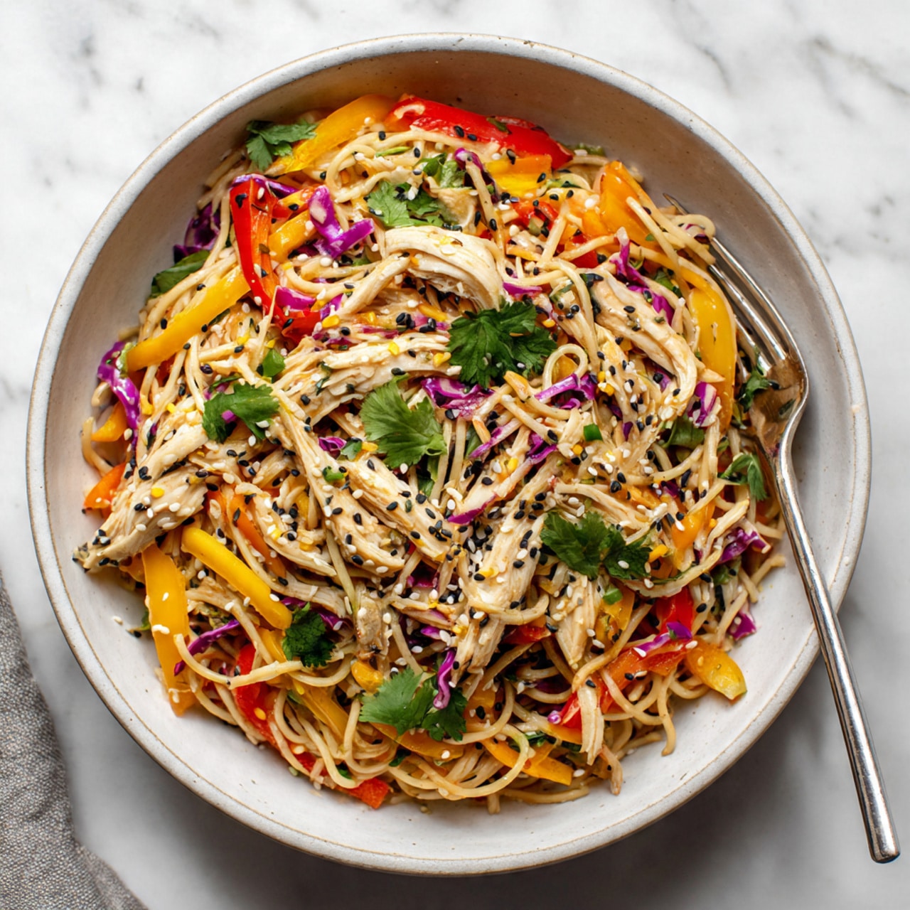 The dish shows three main layers in a white bowl on a white marbled surface. The bottom layer is a tangle of light brown noodles forming a soft bed. Over this, colorful pieces of yellow and red bell peppers and shredded light purple cabbage are spread evenly, adding bright tones. On top, shredded light beige chicken is scattered with fresh green cilantro leaves standing out. Small black and white sesame seeds sprinkle over all layers, giving a fine texture. A silver fork is placed casually inside the bowl near the right edge. Photo taken with an iphone --ar 4:5 --v 7