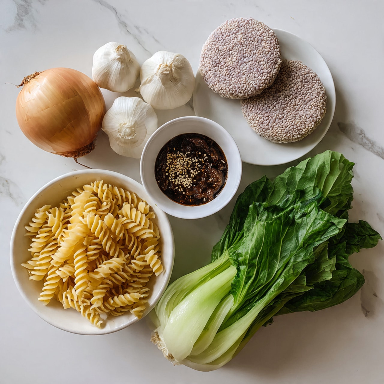 The image shows fresh ingredients on a white marbled surface, including a white bowl filled with a whole onion, two garlic bulbs, and green leafy vegetables on the right side. Next to the bowl, there is a pile of uncooked spiral pasta with a light yellow color. Above the pasta, there is a small white bowl containing a dark brown sauce topped with sesame seeds. In the top right corner, two round rice cakes with a light purple tint are placed on a white plate. Photo taken with an iphone --ar 4:5 --v 7