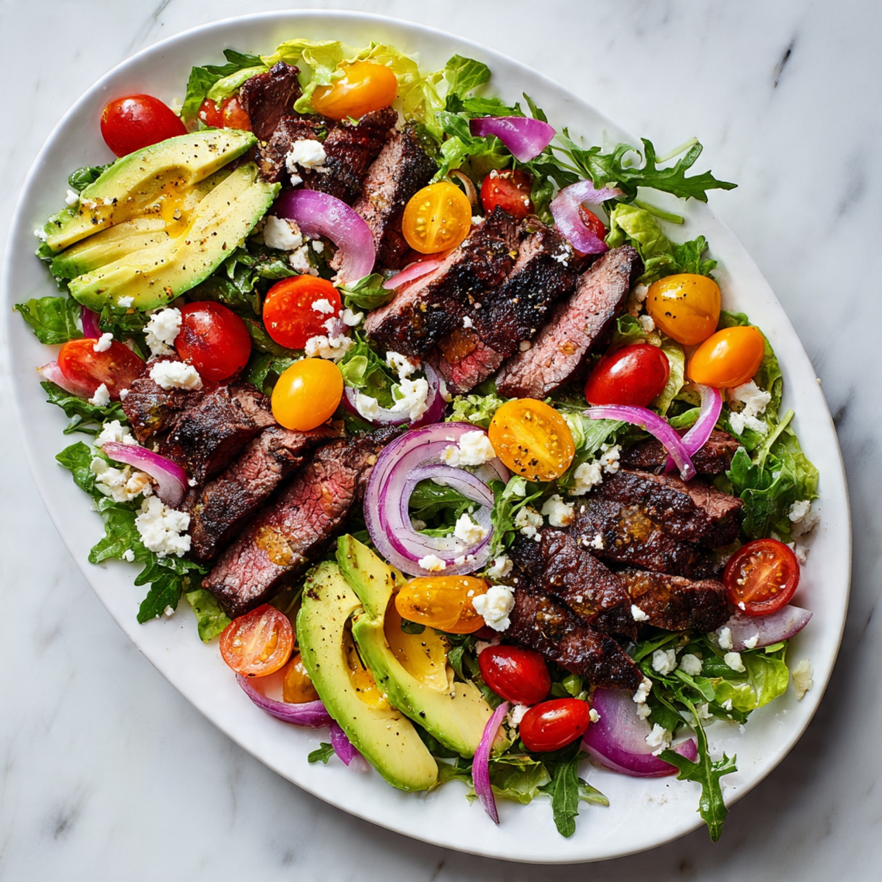 On a large white oval plate, there is a colorful salad layered with fresh green arugula and light yellow lettuce as the base spread evenly across. On top, medium slices of grilled steak with a charred dark brown crust and pink inside are placed in small groups around the plate. Bright orange and red cherry tomato halves are scattered throughout, along with thin rings of light purple pickled onions. Three sections of sliced avocado with a smooth, pale green texture and a drizzle of olive oil and black pepper are arranged around the edges. Small crumbles of white feta cheese are sprinkled over the salad adding a contrasting texture. The plate sits on a white marbled surface with soft lighting enhancing the fresh and vibrant colors. Photo taken with an iphone --ar 4:5 --v 7
