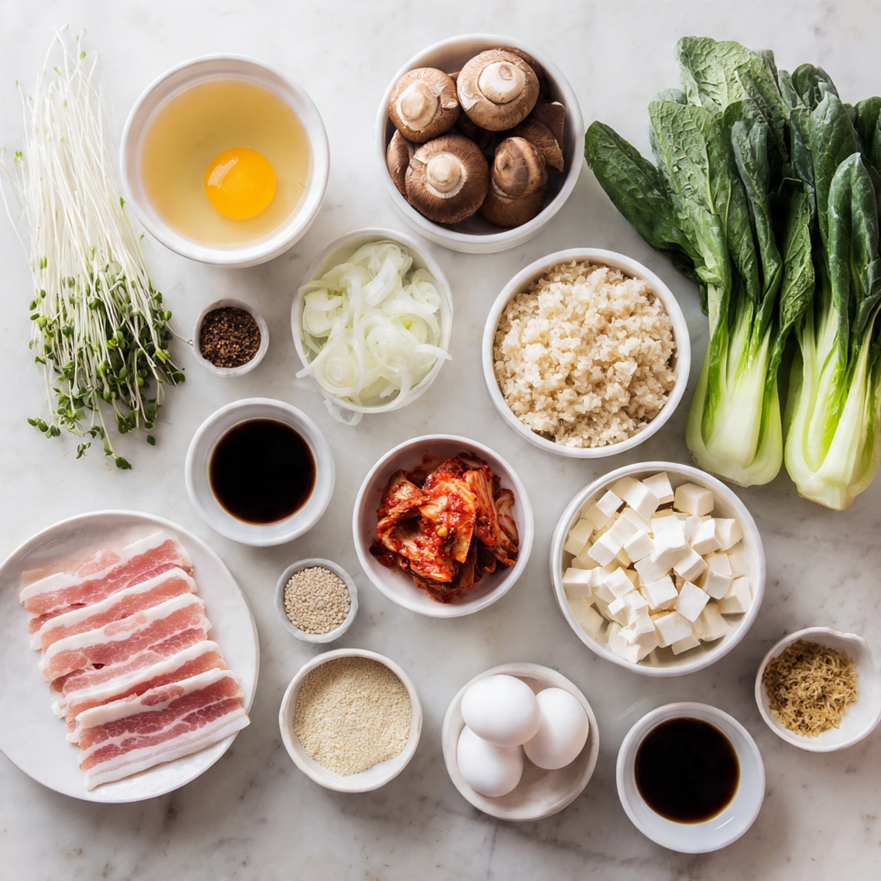 The image shows a white marble surface with many small white bowls and plates arranged neatly, each holding different ingredients. There are thin slices of raw pink pork belly on a white plate in the lower left. Above it, one bowl has fluffy, light brown cooked rice. Next to the rice, fresh green leafy bok choy and brown mushrooms are placed side by side. In the top row, there is a bowl of clear golden broth on the left, a small bowl of thin red kimchi near the center, and two white bowls filled with sliced white onions and small white eggs on the right. Scattered around are tiny bowls containing dark soy sauce, chopped white garlic, sesame seeds, and small cubes of white tofu. A woman's hand is lifting some green sprouts near the rice. The scene is bright with a clean, fresh look, photo taken with an iphone --ar 4:5 --v 7