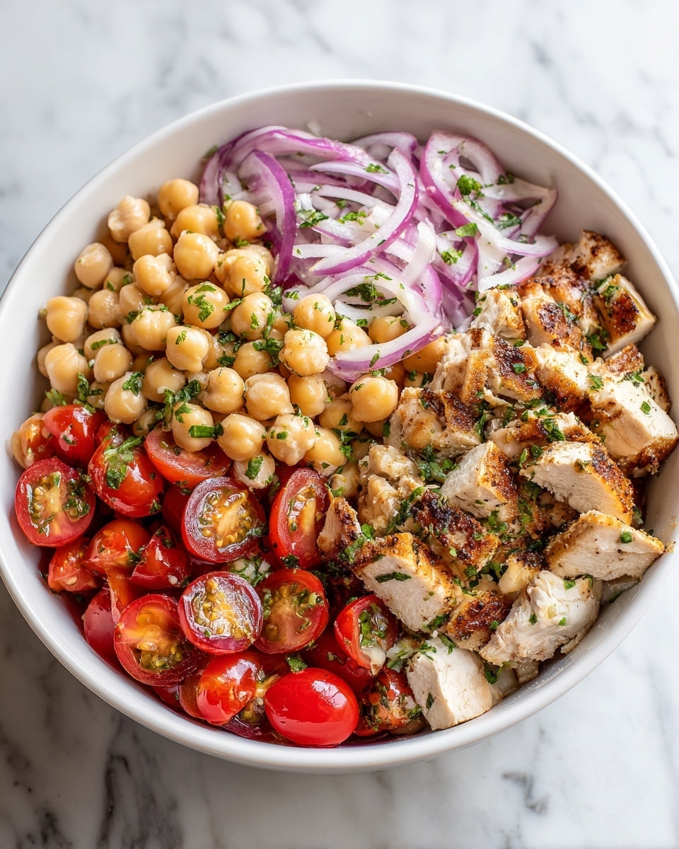 A white bowl filled with a layered salad consisting of light beige cooked chickpeas as the base layer, topped with pieces of light brown grilled chicken, halved bright red cherry tomatoes, thin slices of purple onion, and chopped green herbs scattered evenly on top. The colors are vibrant and fresh, with the textures showing the softness of chickpeas, juiciness of tomatoes, and slight crispness of onions. The bowl sits on a white marbled surface. Photo taken with an iphone --ar 4:5 --v 7