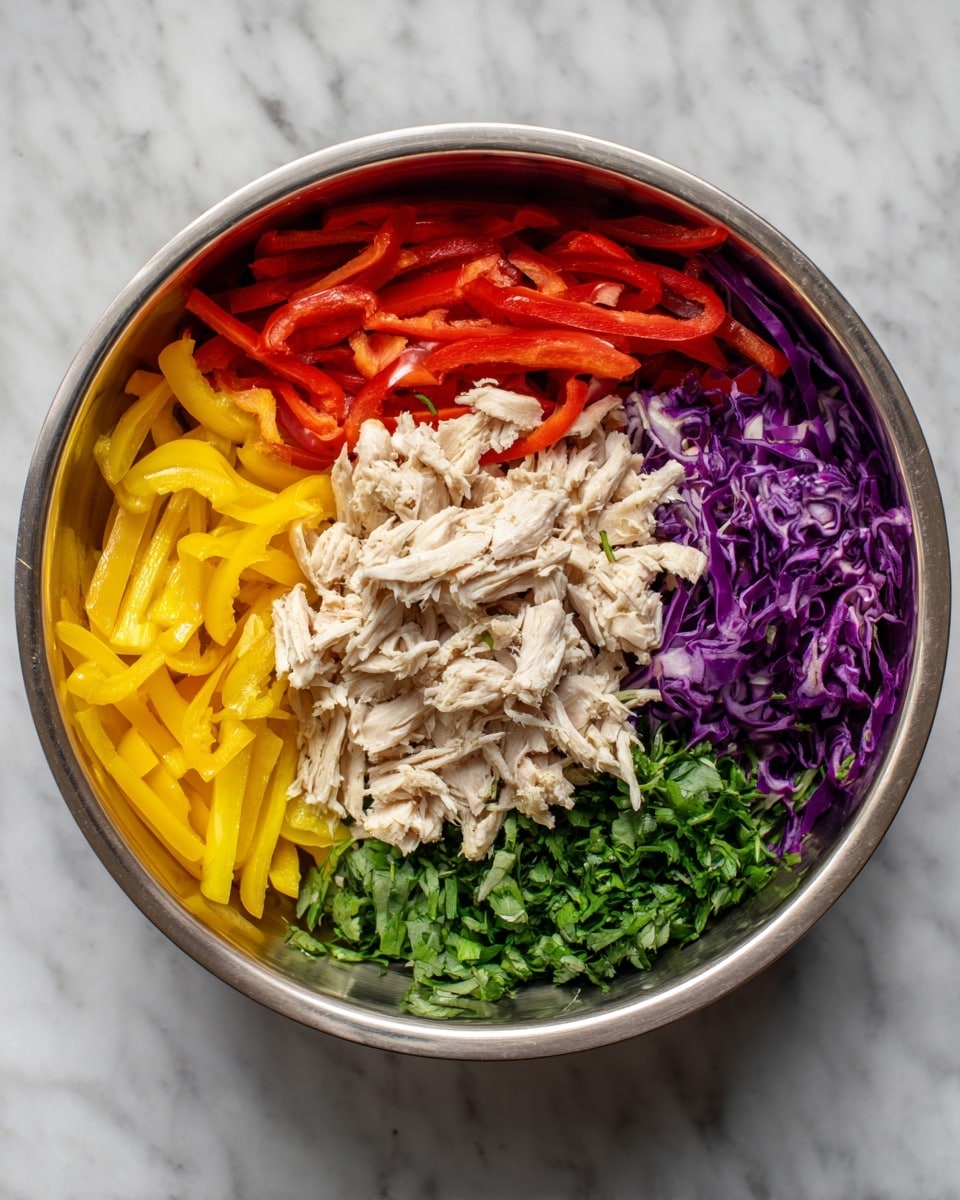 A silver bowl shows five layers of food neatly placed side by side. Starting from the left, there are bright yellow bell pepper strips, next to them are red bell pepper strips, followed by a pile of shredded light beige chicken in the center. To the right of the chicken, there is a bunch of chopped green herbs, and finally, purple shredded cabbage on the far right. The bowl sits on a white marbled surface. photo taken with an iphone --ar 4:5 --v 7