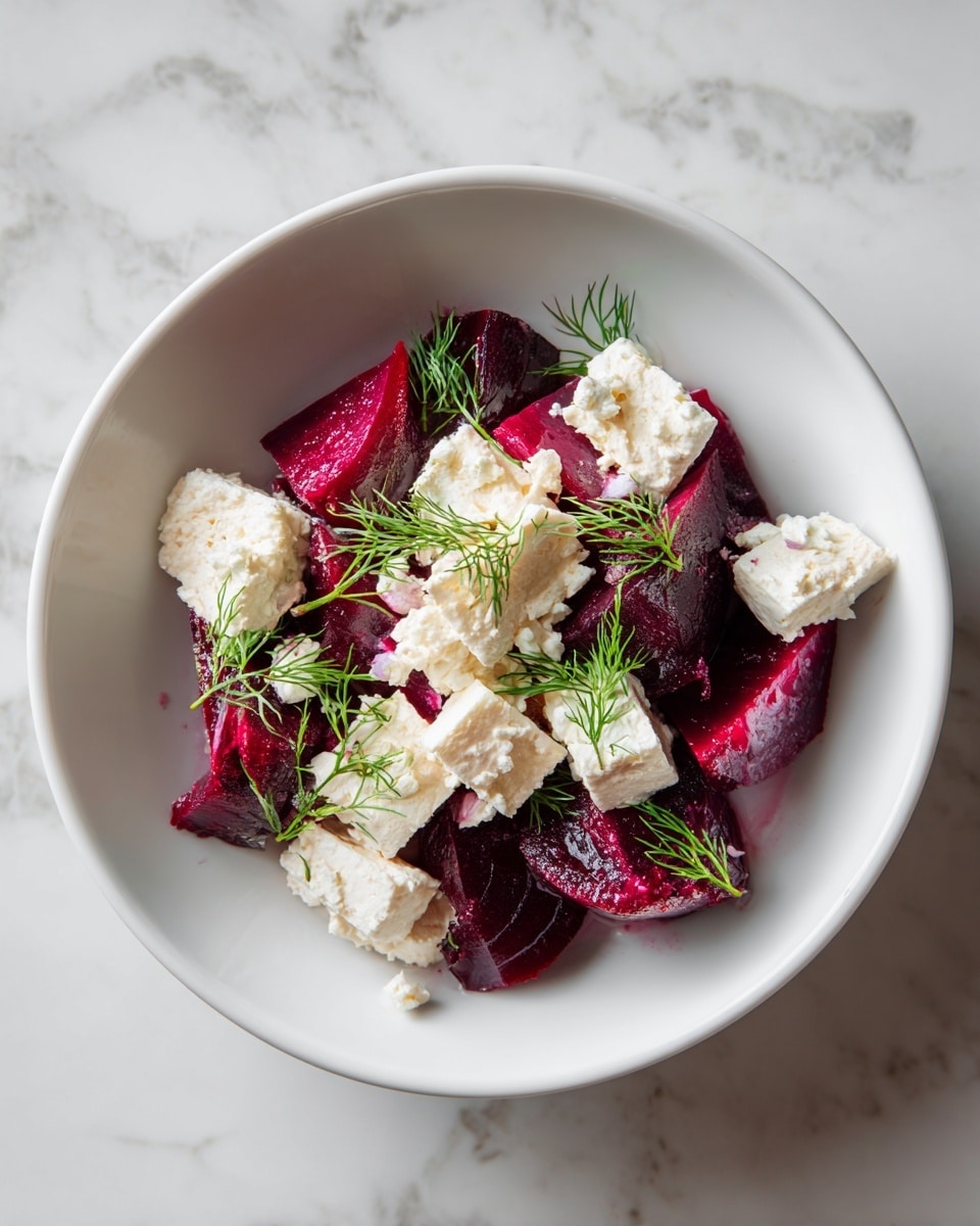 A white bowl contains a salad with several layers: at the bottom, there are deep red beet slices, thin and stacked loosely, creating a textured base; on top of the beets, there are soft, white chunks of cheese spread unevenly; scattered around the cheese are small sprigs of fresh, bright green dill, giving a fresh look; the bowl sits on a white marbled surface. photo taken with an iphone --ar 4:5 --v 7