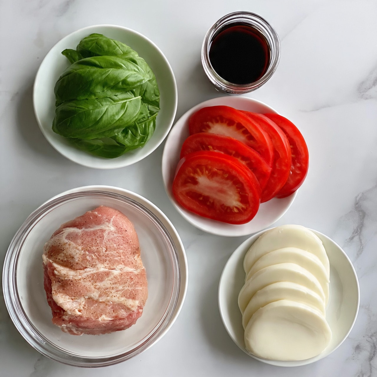 square image The image shows five white plates and bowls placed on a white marbled surface. The largest clear bowl at the bottom left holds a piece of light pink seasoned raw meat. Above it, a small white plate contains bright green fresh basil leaves, layered loosely. To the right, there is a small glass jar filled with dark brown balsamic vinegar. Below the jar, a white plate displays five thick slices of red tomato arranged in a single layer, overlapping slightly. Finally, to the far right, another white plate holds six smooth, round white cheese slices stacked neatly. Photo taken with an iphone --ar 4:5 --v 7