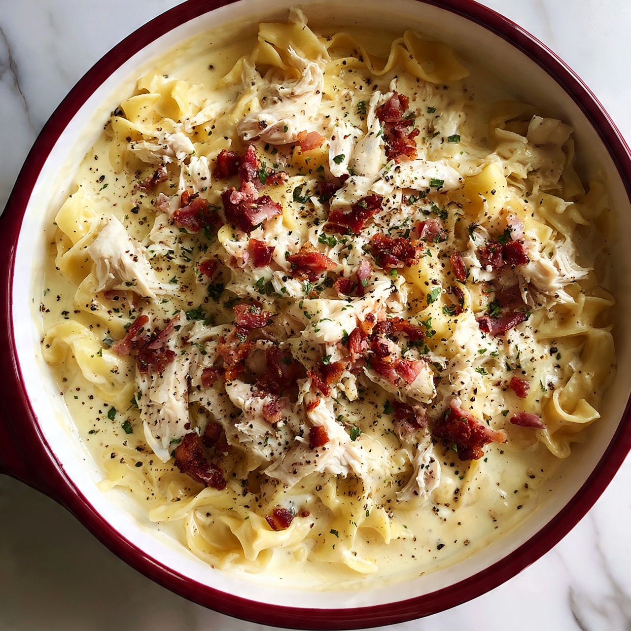 square image The dish is served in a deep red pot with a white inside, placed on a white marbled surface. The base layer is wide egg noodles submerged in a creamy light yellow sauce that has an inviting smooth texture. On top of the noodles, there are scattered pieces of shredded white chicken and small chunks of crispy bacon, adding reddish-brown and pinkish tones. The dish is sprinkled with chopped green herbs and some cracked black pepper, giving spots of green and black over the creamy and light brown colors. The whole presentation looks warm and hearty, showing a mix of creamy, soft noodles and crispy bacon bits. photo taken with an iphone --ar 4:5 --v 7
