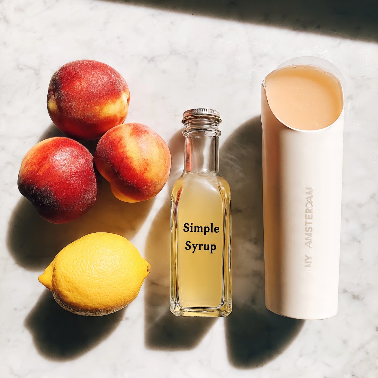 square image The image shows four food items placed on a white marbled surface. On the left side, there are two peaches with red and orange skin and one bright yellow lemon below them. In the middle, there is a clear glass bottle labeled