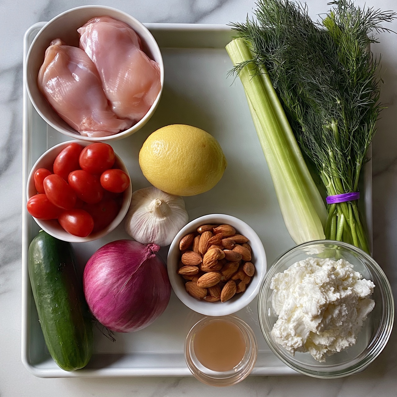 square image A baking tray holds various fresh ingredients arranged neatly on a white marbled surface. In the top left corner, there is a white bowl with two raw pink chicken pieces. Below it, a smaller white bowl is filled with bright red grape tomatoes. Towards the bottom left, a dark green cucumber lies next to a whole purple red onion. In the center, a single yellow lemon rests beside a bulb of garlic. To the right of the lemon, another white bowl contains brown almonds. On the right side of the tray, a long stalk of light green celery leans against a bunch of fresh dark green dill tied with a purple band. At the bottom right corner, a clear glass bowl holds a mound of white ricotta cheese. A small clear cup with a light brown liquid sits near the cucumber. photo taken with an iphone --ar 4:5 --v 7