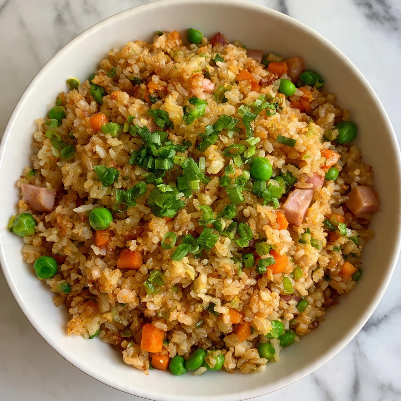 square image A white bowl filled with fried rice containing several layers of ingredients: light brown cooked rice mixed with small orange carrot cubes, bright green peas, chopped green onions scattered on top, and small pieces of light pink ham. The texture looks soft and slightly crispy with a colorful mix of vegetables and meat. The bowl is placed on a white marbled surface. Photo taken with an iphone --ar 4:5 --v 7