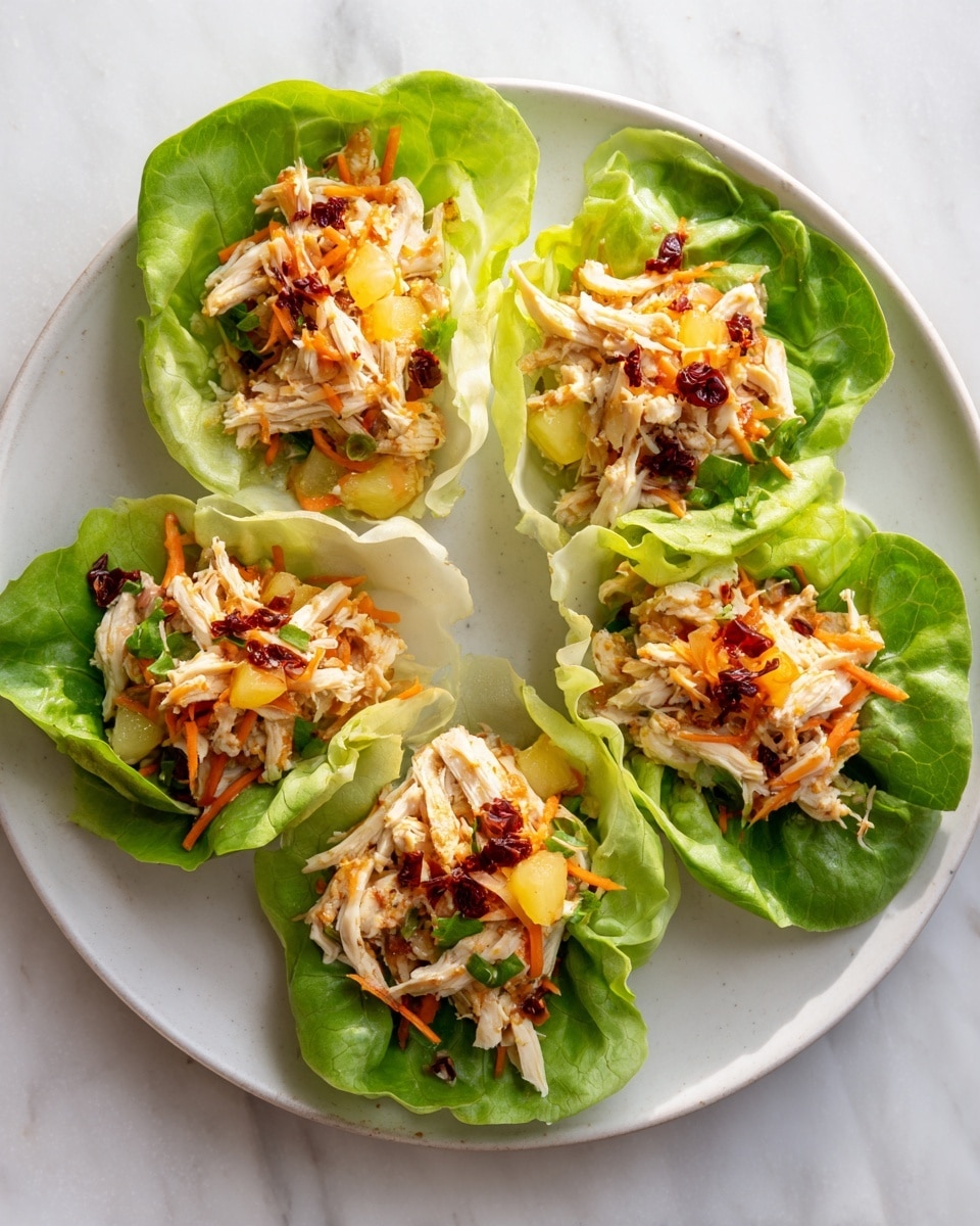 Five lettuce cups are arranged in a circle on a large white plate. Each cup has a bright green leaf of lettuce forming a small bowl. Inside each lettuce cup is a mix of light shredded chicken, thin orange carrot strips, and small chunks of light yellow fruit or vegetable. The mixture is topped with small dark red flakes. The white plate sits on a white marbled surface with soft natural light. Photo taken with an iphone --ar 4:5 --v 7