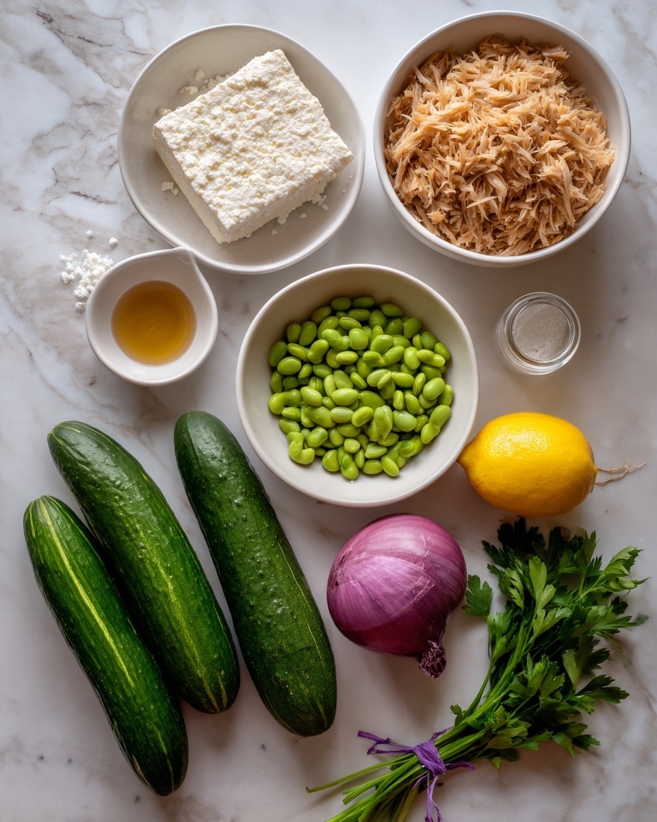 The image shows ingredients neatly placed on a white marbled surface. There is one white bowl filled with light brown flakes resembling shredded tuna, another white bowl with light brown rice grains, and a third white bowl holding green edamame beans. Next to these are two smooth, dark green cucumbers laying side by side. A block of crumbly white cheese is placed above the shredded tuna. A small white dish holds a golden liquid, likely oil or vinegar, while a tiny glass jar contains a darker amber liquid. A bright yellow lemon and a whole red onion with its purple skin intact sit nearby. A bunch of fresh green parsley with leafy stems is tied with a purple elastic band in the lower right corner. The overall look is fresh, clean, and ready for cooking. photo taken with an iphone --ar 4:5 --v 7