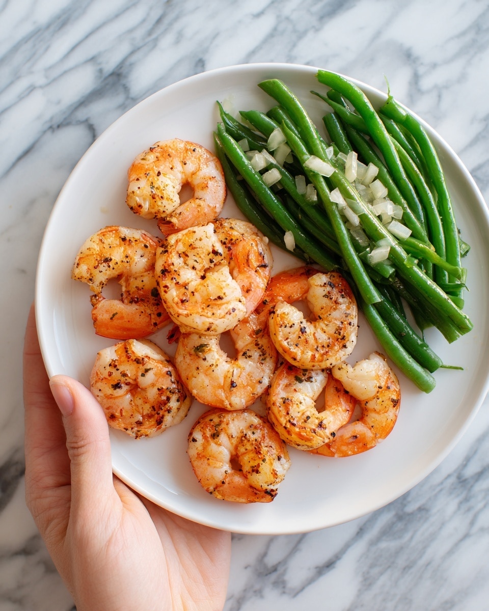 A white plate on a white marbled surface holds six cooked shrimp arranged in a circular pattern near the edge. The shrimp are pinkish-orange with visible grill marks and light seasoning. In the center of the plate, there is a small pile of green beans and pale strips of diced vegetables mixed together, creating a fresh and colorful contrast to the shrimp. A woman's hand is shown gently holding the edge of the plate. Photo taken with an iphone --ar 4:5 --v 7