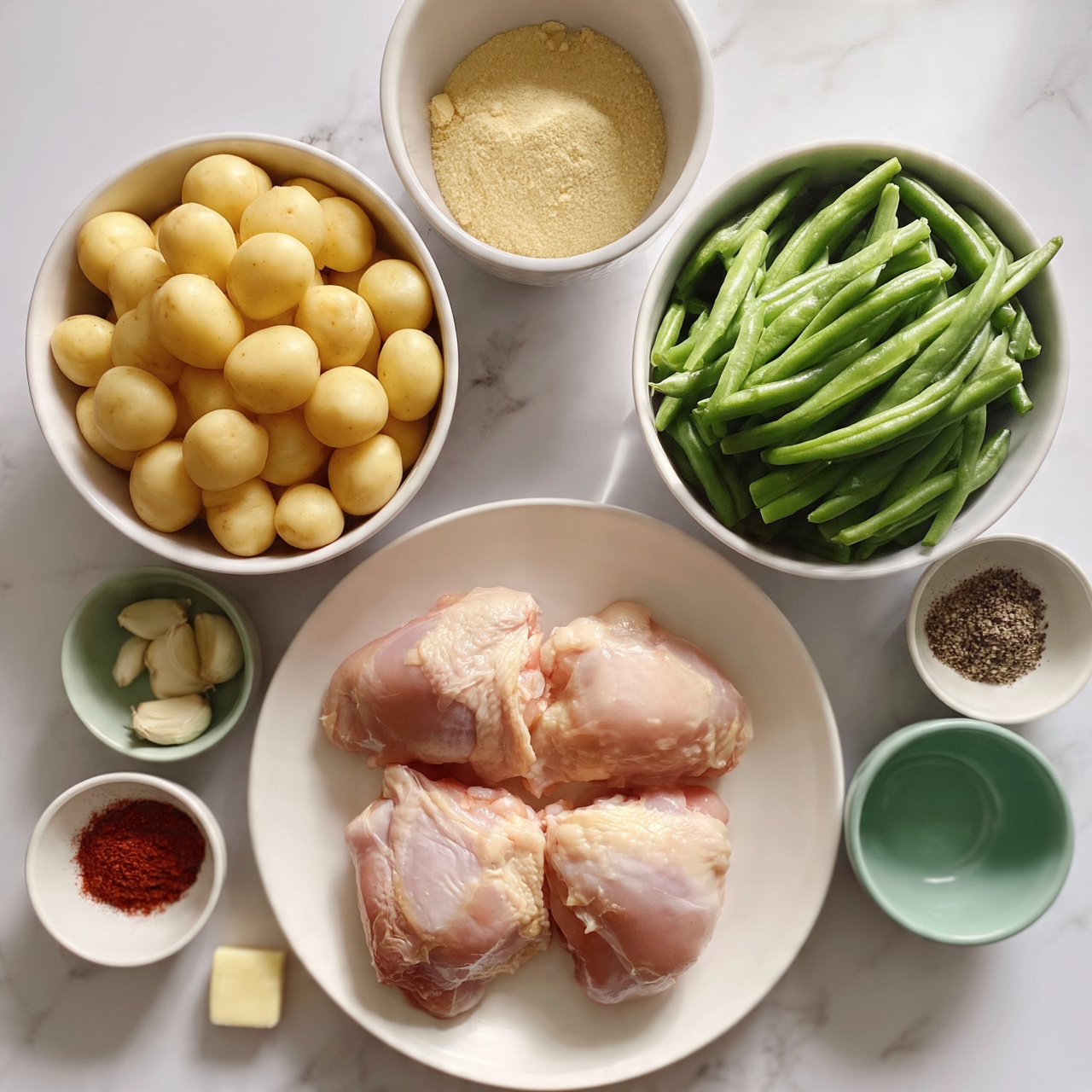 square image The image shows several bowls and a white plate arranged neatly on a white marbled surface. In the center bottom, a white plate holds four raw chicken thighs with soft pink color and light skin texture. To the top left, there is a white bowl filled with many small round yellow potatoes. Above that, a white bowl contains a light yellow powder, likely a seasoning. On the top right, a white bowl is full of fresh green beans, their smooth and shiny texture visible. Surrounding these are small white and green bowls holding garlic cloves, ground spices including black pepper and red paprika, a small square piece of butter, and an empty green bowl. The whole setting looks clean and organized, with soft natural light highlighting the colors and textures photo taken with an iphone --ar 4:5 --v 7