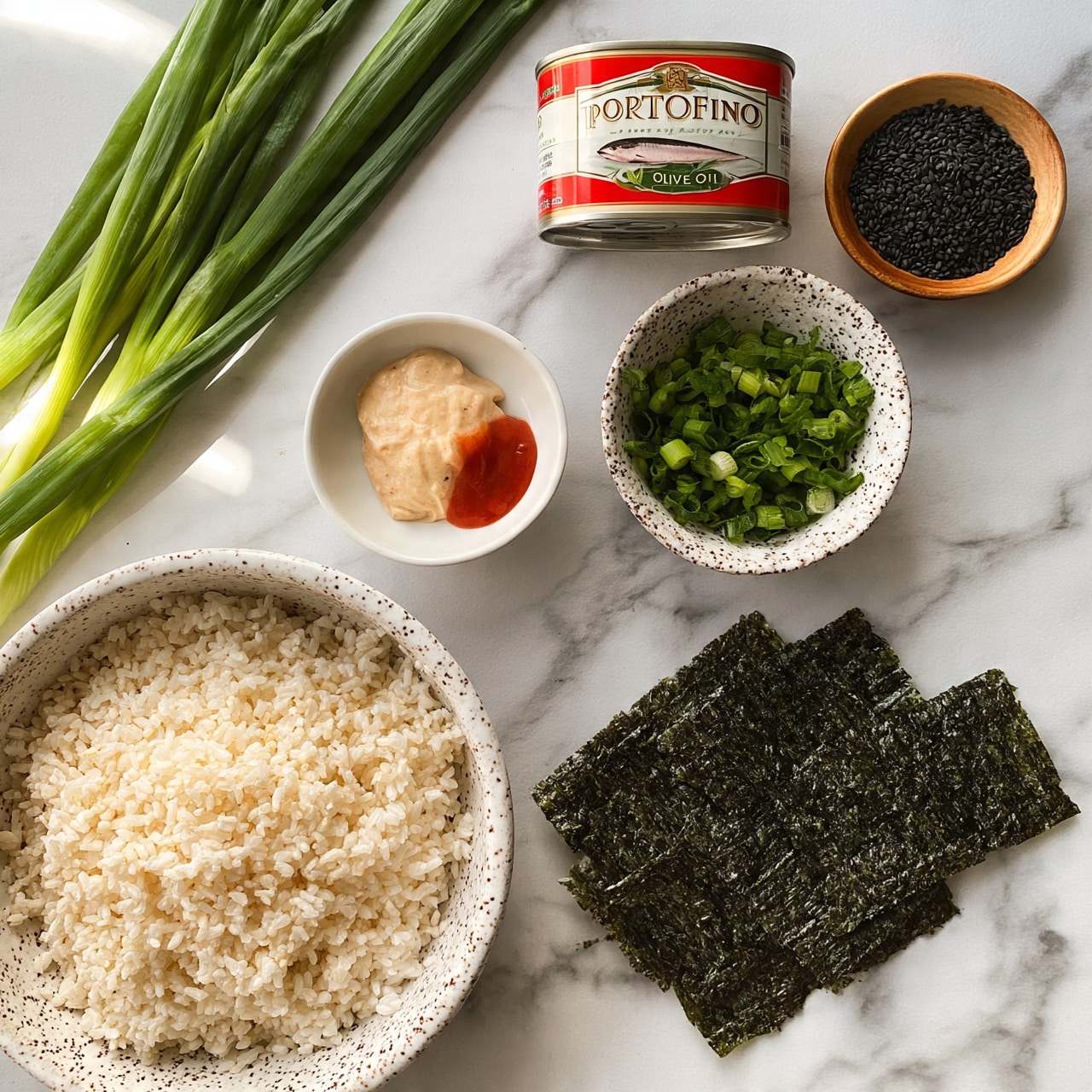 square image The image shows several ingredients arranged neatly on a white marbled surface. In the bottom left, there is a large speckled white bowl filled with uncooked white rice. To the right of that, on the white marbled surface, are three dark green rectangular sheets of seaweed. Above the rice bowl, there is a small white bowl containing a dollop of light beige sauce and some red sauce. To the right of this bowl, there is a speckled white bowl filled with chopped green onions. Above the green onions, there is an unopened can of Portofino tuna in olive oil with a red and white label. To the right of the tuna can, a small wooden bowl holds black sesame seeds. Some fresh green onions with long green stalks are positioned diagonally in the upper left corner. The overall setting is bright and clear, with natural lighting present. Photo taken with an iphone --ar 4:5 --v 7