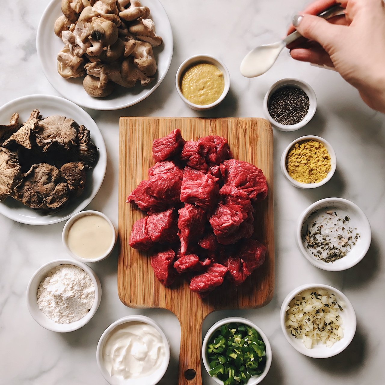 square image The image shows a wooden cutting board in the center with bright red slices of raw meat piled on it, surrounded by various small white bowls and plates arranged on a white marbled surface. To the top left, there is a white plate full of light brown sliced mushrooms, and below it, another white plate with larger, darker dried mushrooms. Around the board, there are small white bowls containing light yellow mustard, black pepper, yellowish ground spice, flour, a creamy white sauce, sour cream, chopped green chilies, finely chopped onions, and some herbs, all set neatly in a flat lay style. A woman's hand holds a spoon dipping in white sauce on the top right. The colors are soft and natural. Photo taken with an iphone --ar 4:5 --v 7