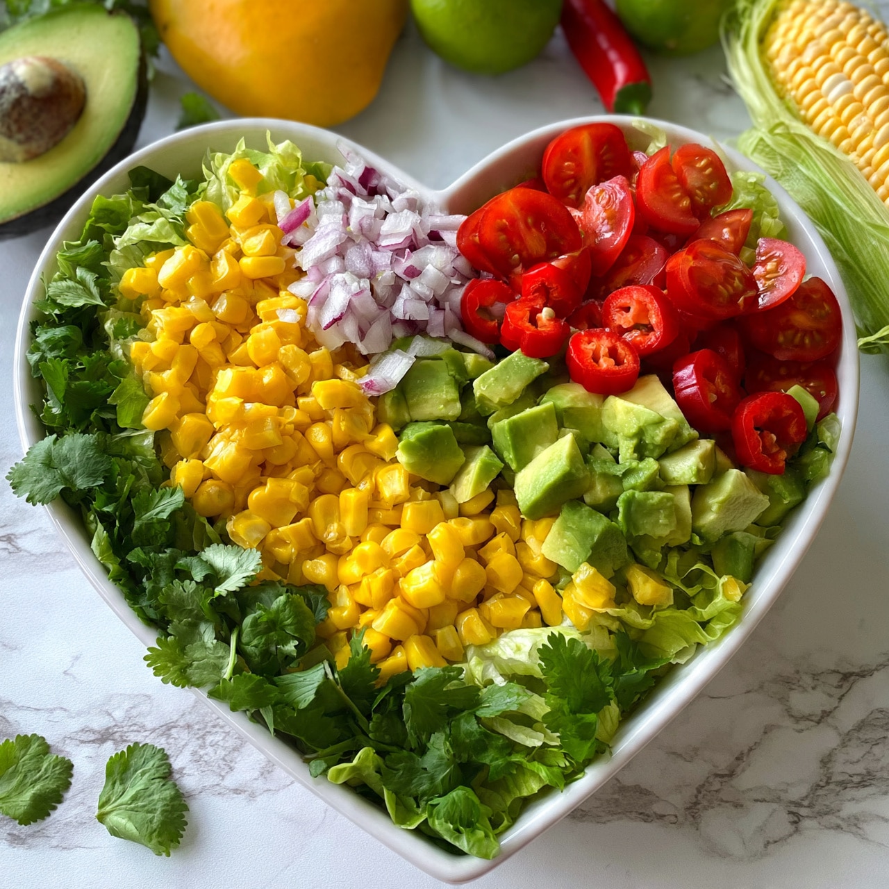 square imageA heart-shaped white bowl filled with a layered salad. The bottom layer has a mix of chopped green lettuce and cilantro leaves that spread evenly. On top, there are bright yellow corn pieces, red cherry tomato halves, red chili slices, chopped red onion, and diced green avocado. The colors are fresh and vivid with green, red, and yellow standing out clearly. The bowl is placed on a white marbled surface with a half avocado, a yellow mango, a lime, a chili, and a fresh corn cob nearby, adding natural and colorful elements to the scene. Photo taken with an iphone --ar 4:5 --v 7