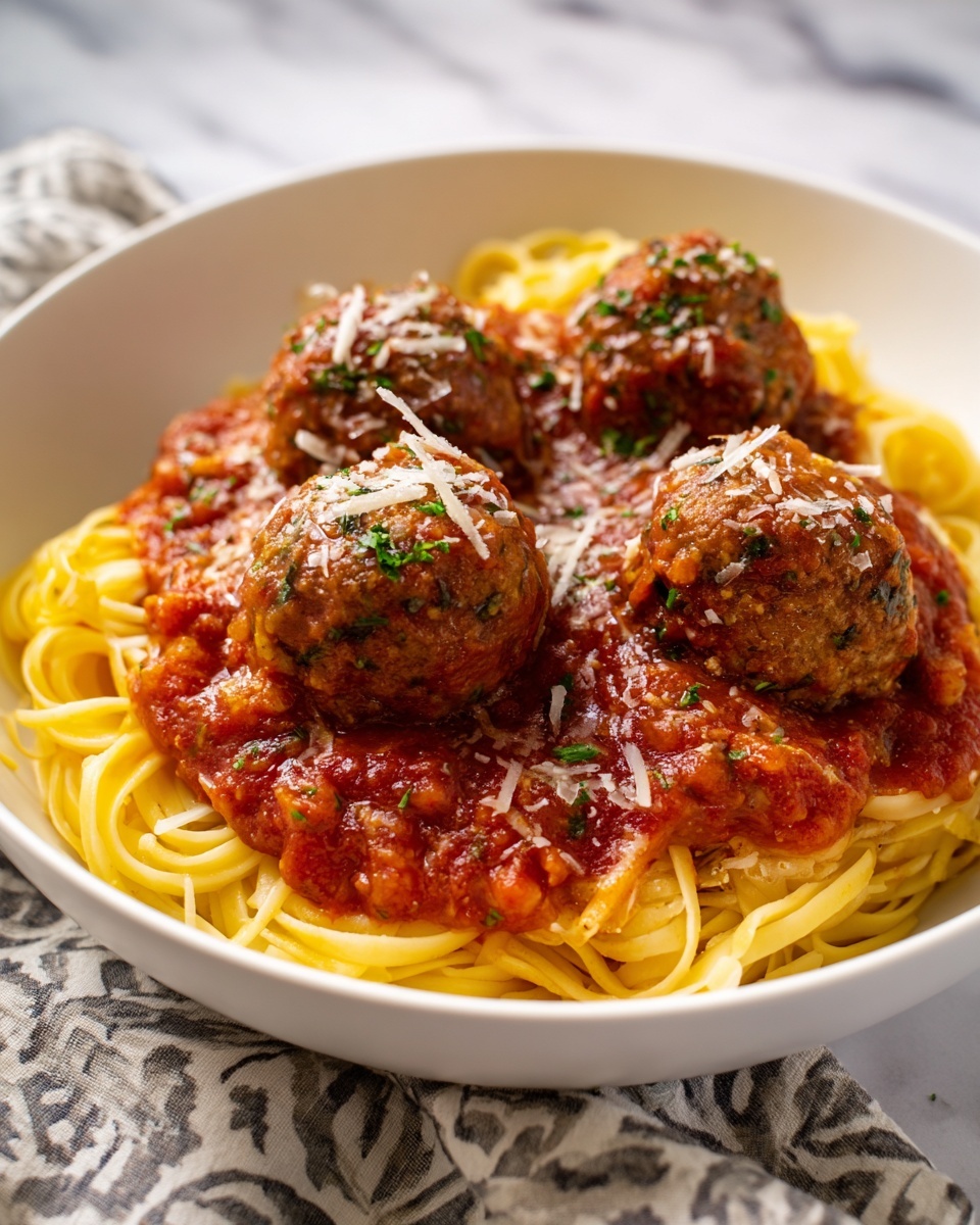 A white bowl is filled with a base layer of long, thin yellow spaghetti noodles arranged in a loose pile. On top of the pasta is a thick layer of rich red tomato sauce with visible chunks of tomatoes and small bits of onion. Three large, round brown meatballs sit evenly spaced on the sauce, slightly coated by it. The meatballs have a textured surface showing herbs and cooked bits inside. The dish is sprinkled with thin, light-colored grated cheese all over the meatballs and sauce. The bowl sits on a white marbled surface with a patterned cloth partially visible underneath. Photo taken with an iphone --ar 4:5 --v 7